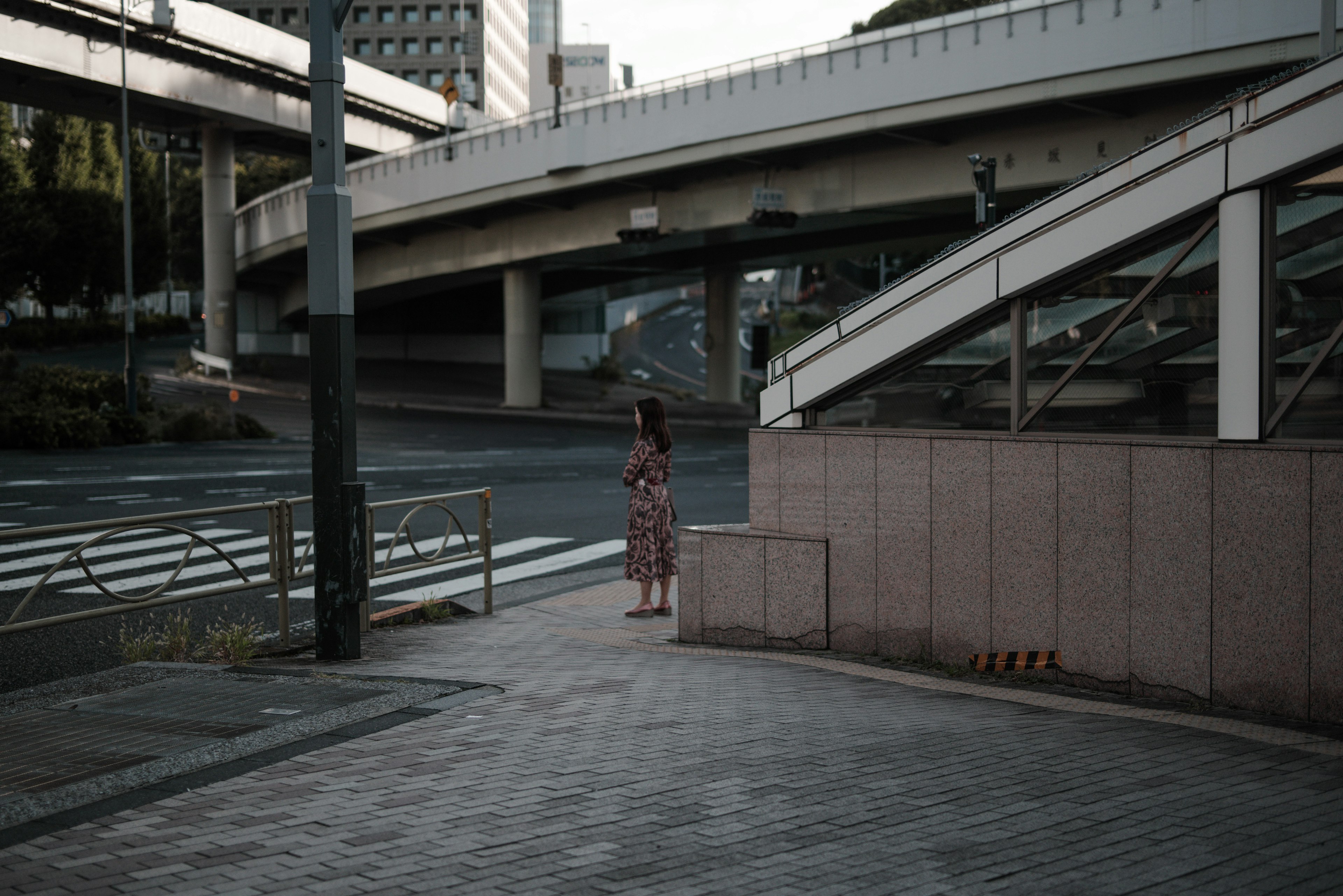 A cityscape featuring a woman standing on the sidewalk