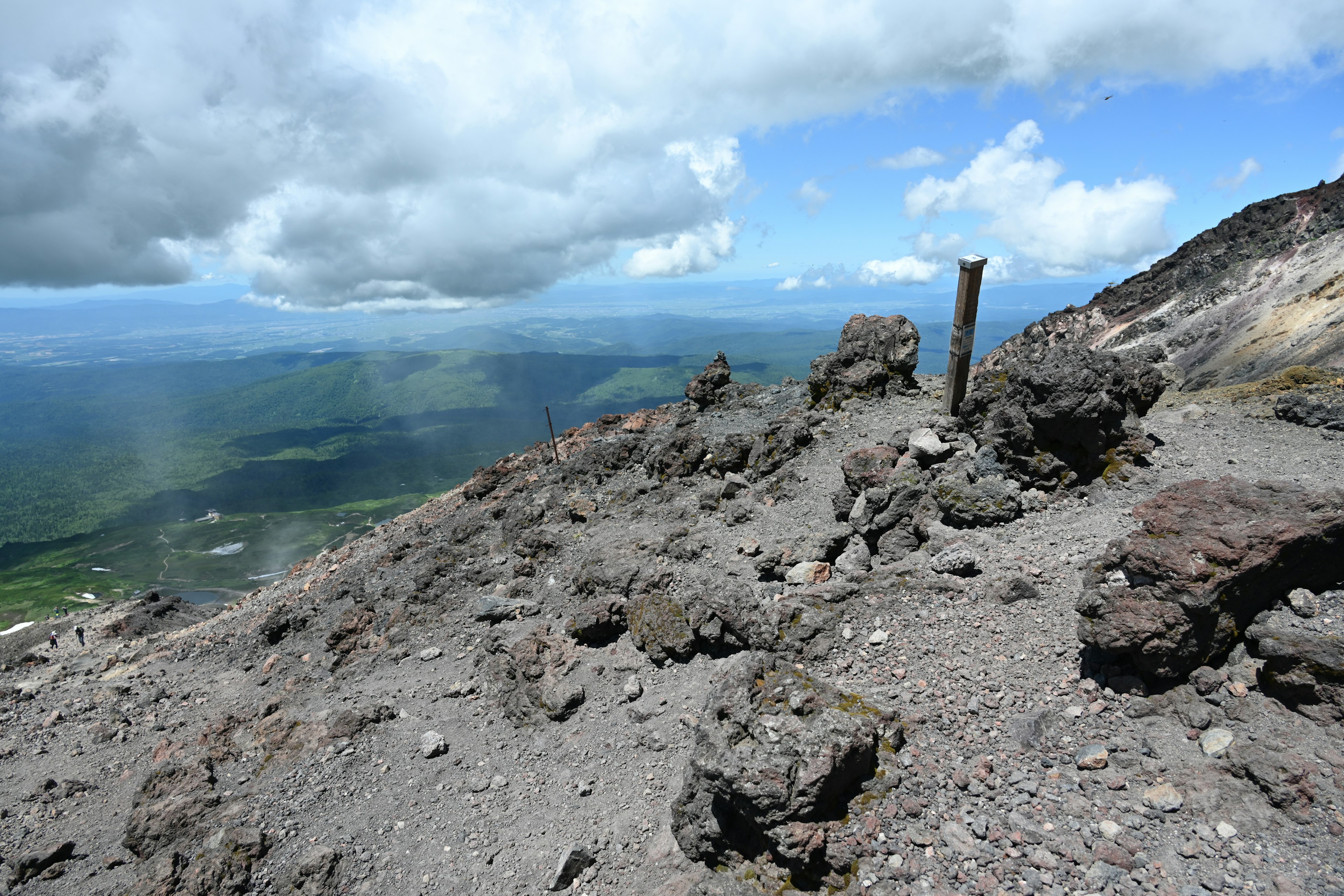 Vue du sommet d'un volcan montrant un terrain rocheux et un ciel bleu avec des nuages