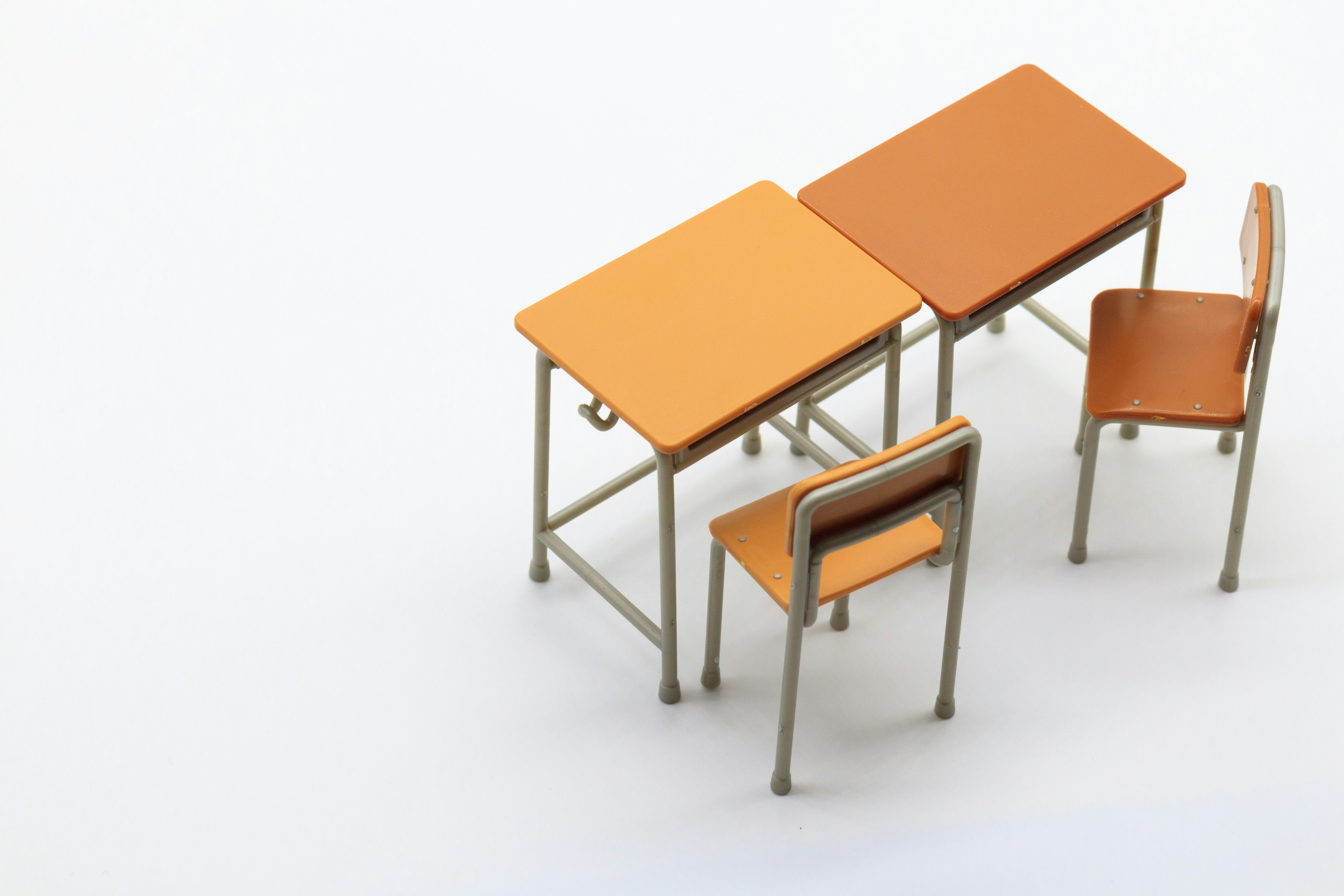 Two orange desks and a chair arranged in a simple classroom scene