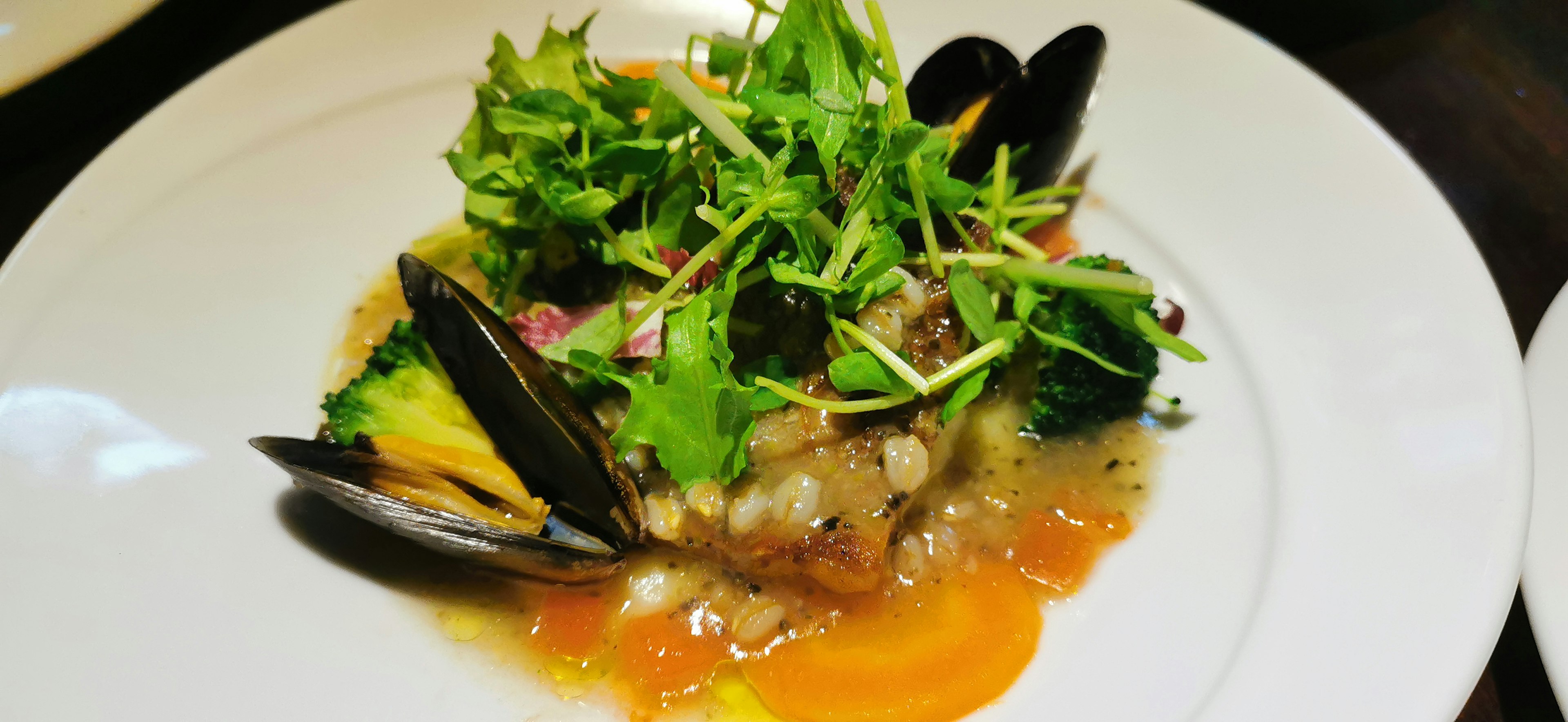 A beautifully plated fish dish with fresh greens and mussels