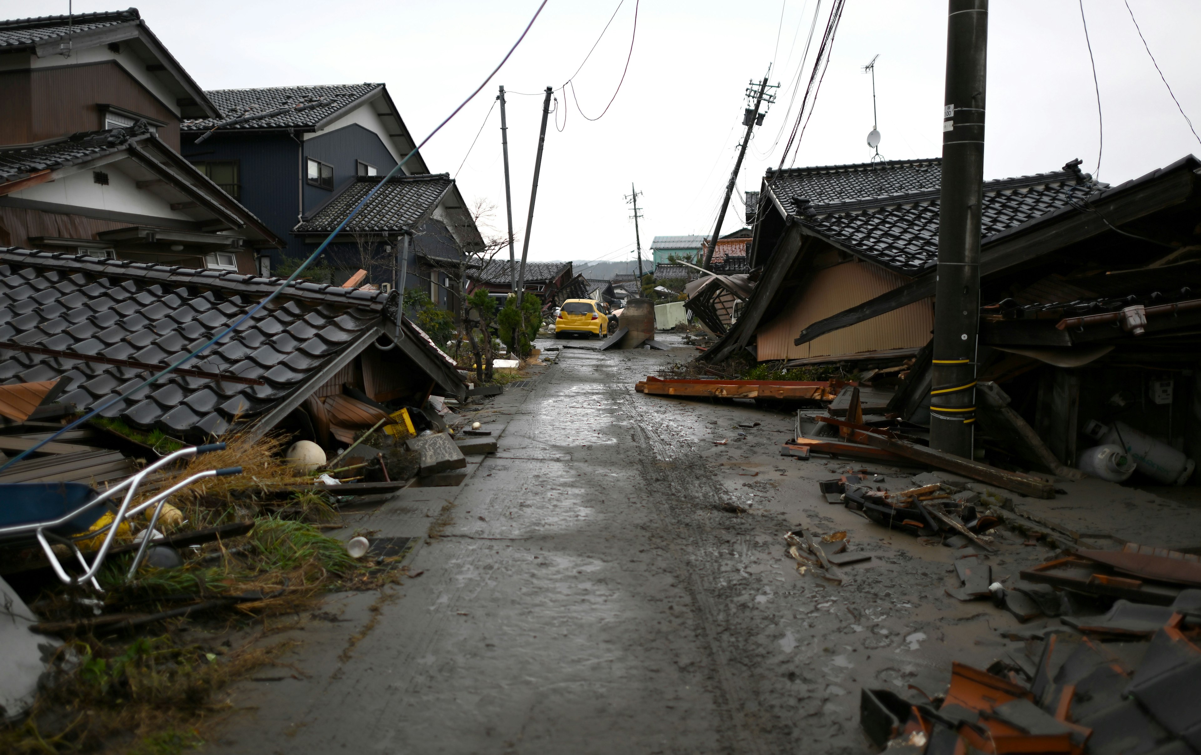 A scene of a damaged street with leaning houses and fallen power poles