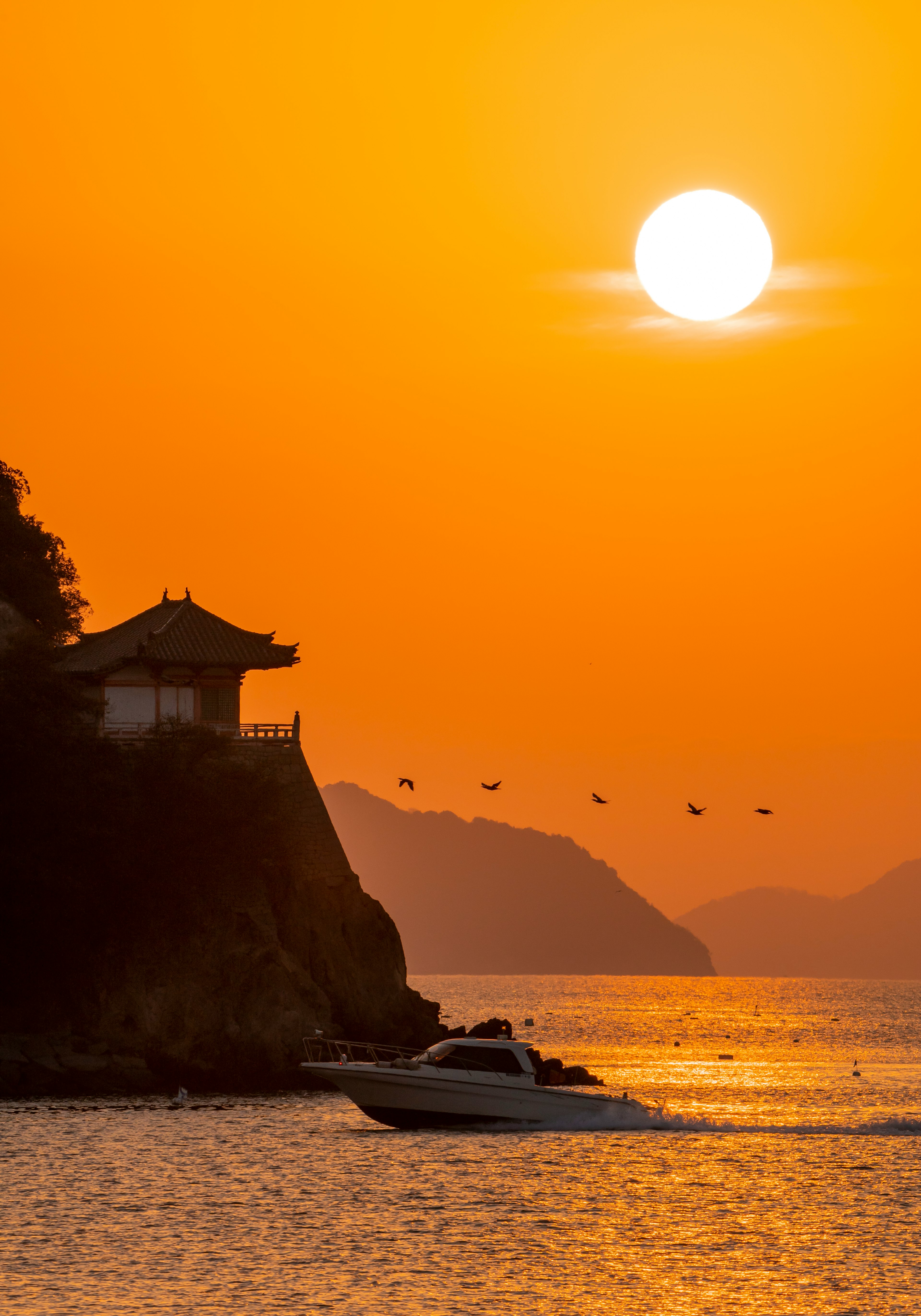 Scène de coucher de soleil côtier avec silhouette d'un bâtiment et d'un bateau