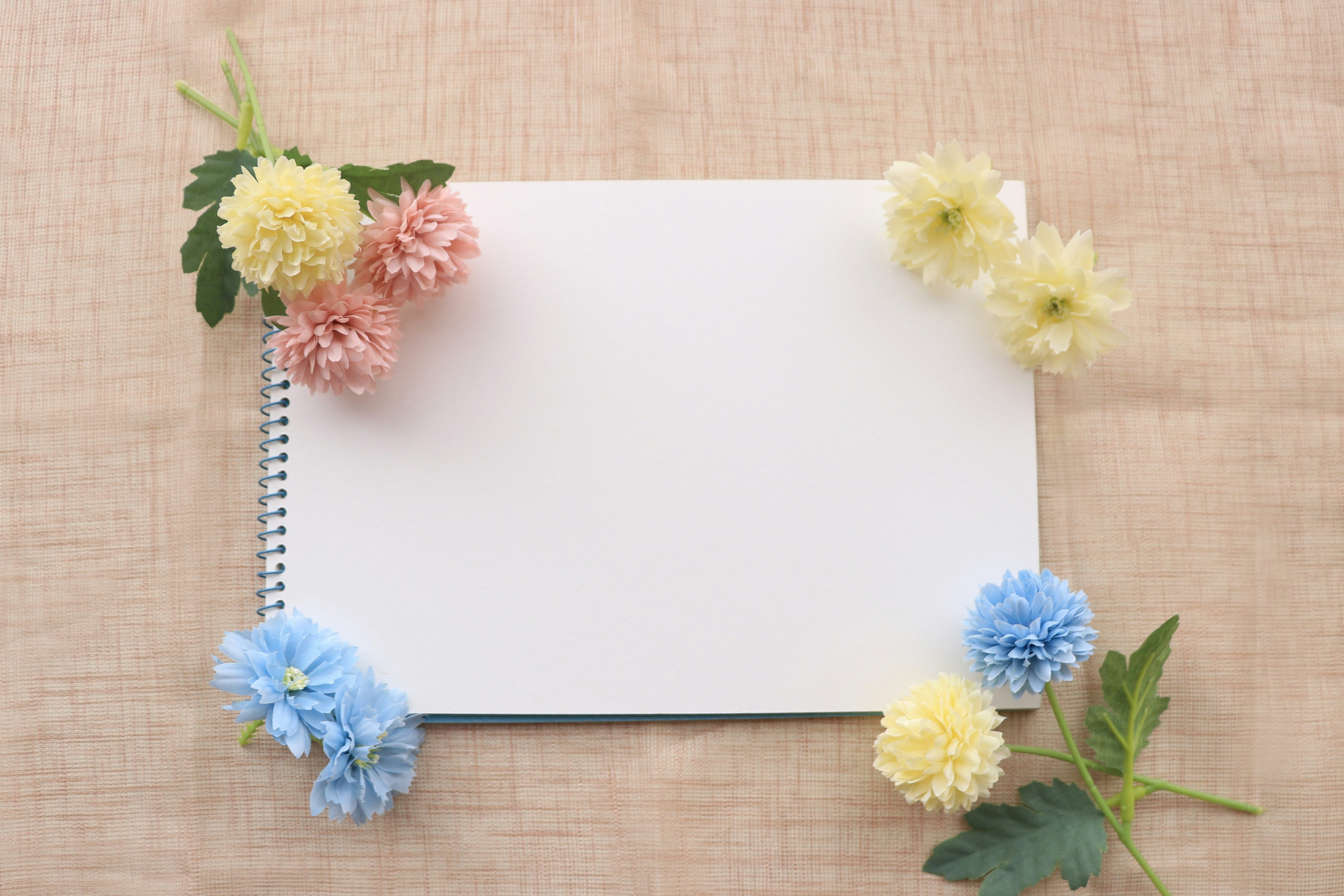 A blank notebook surrounded by colorful flowers on a textured background