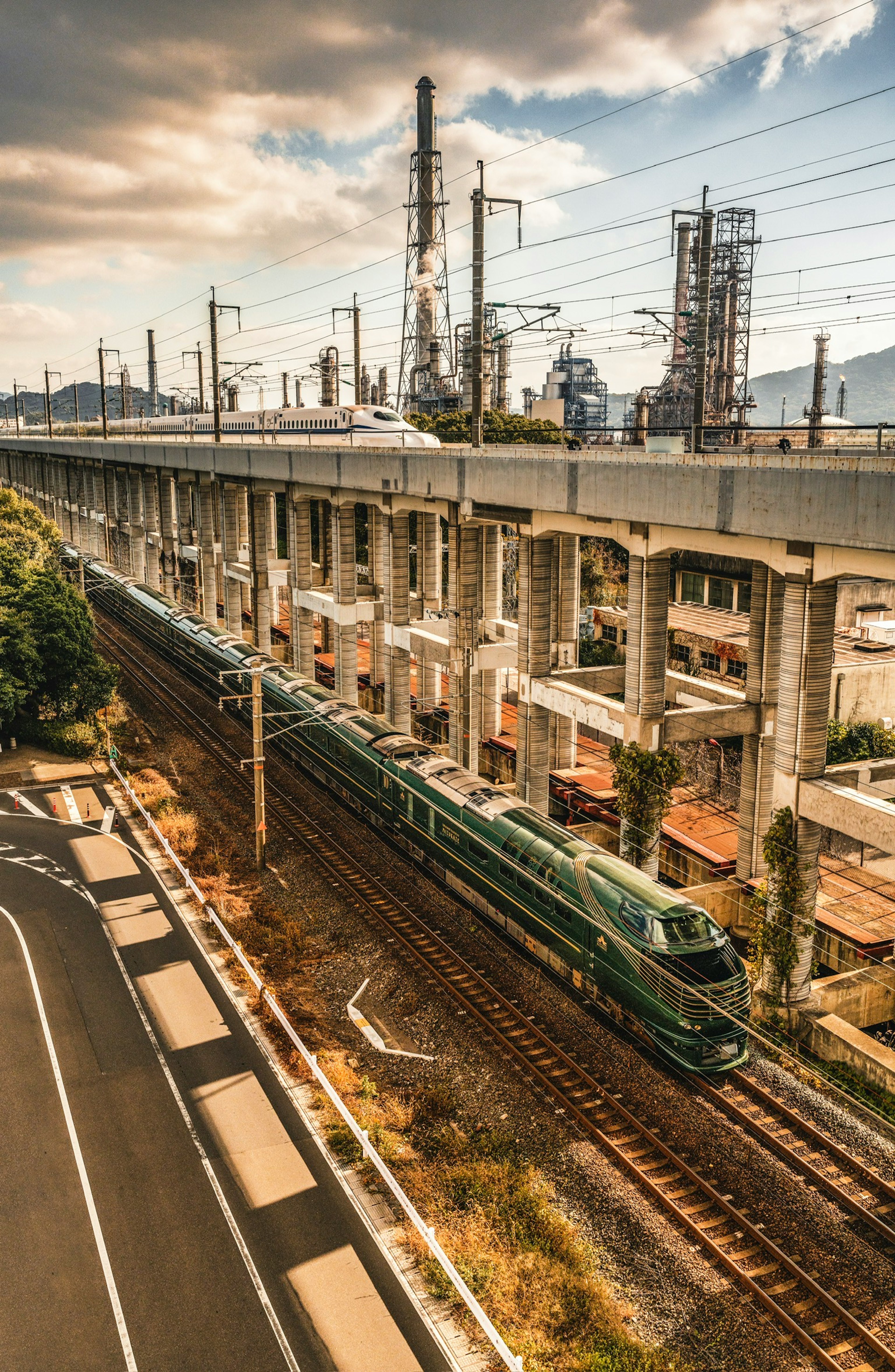 A scenic view featuring railway tracks and an elevated highway a green train travels along the tracks