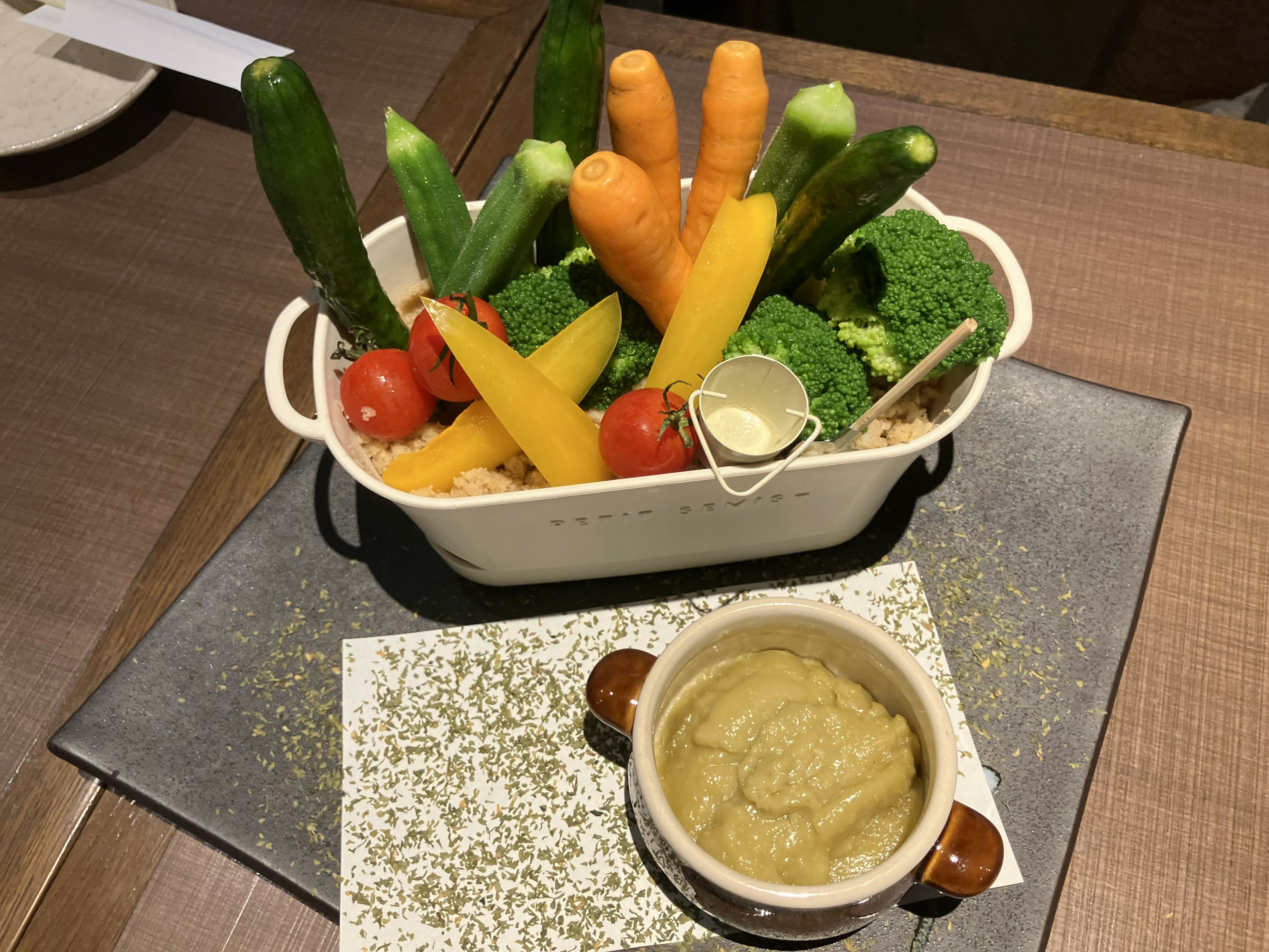 Una bandeja de verduras coloridas que incluyen calabacines zanahorias y brócoli servido con una salsa