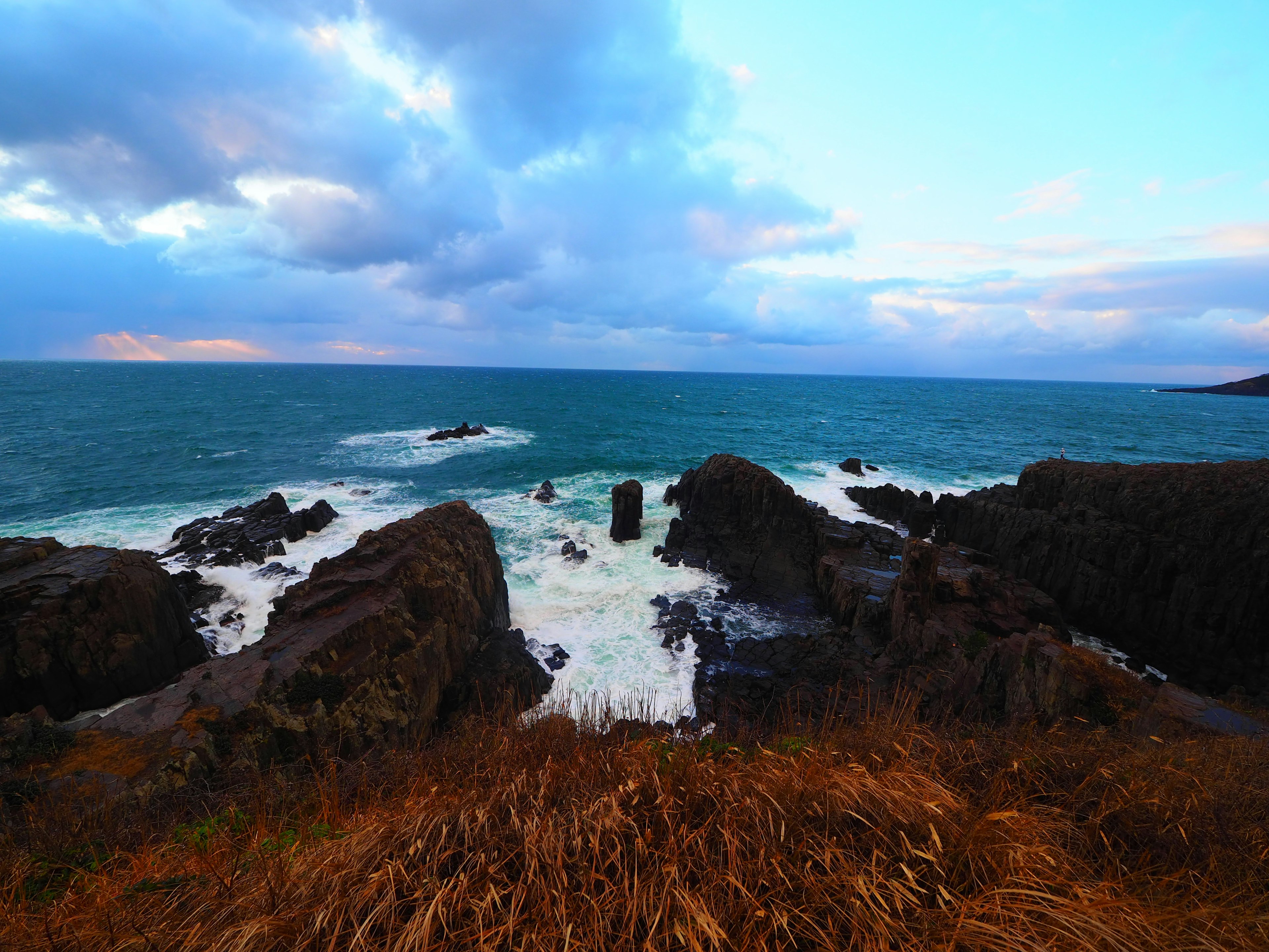 Pemandangan pantai dengan batu dan ombak di bawah langit mendung