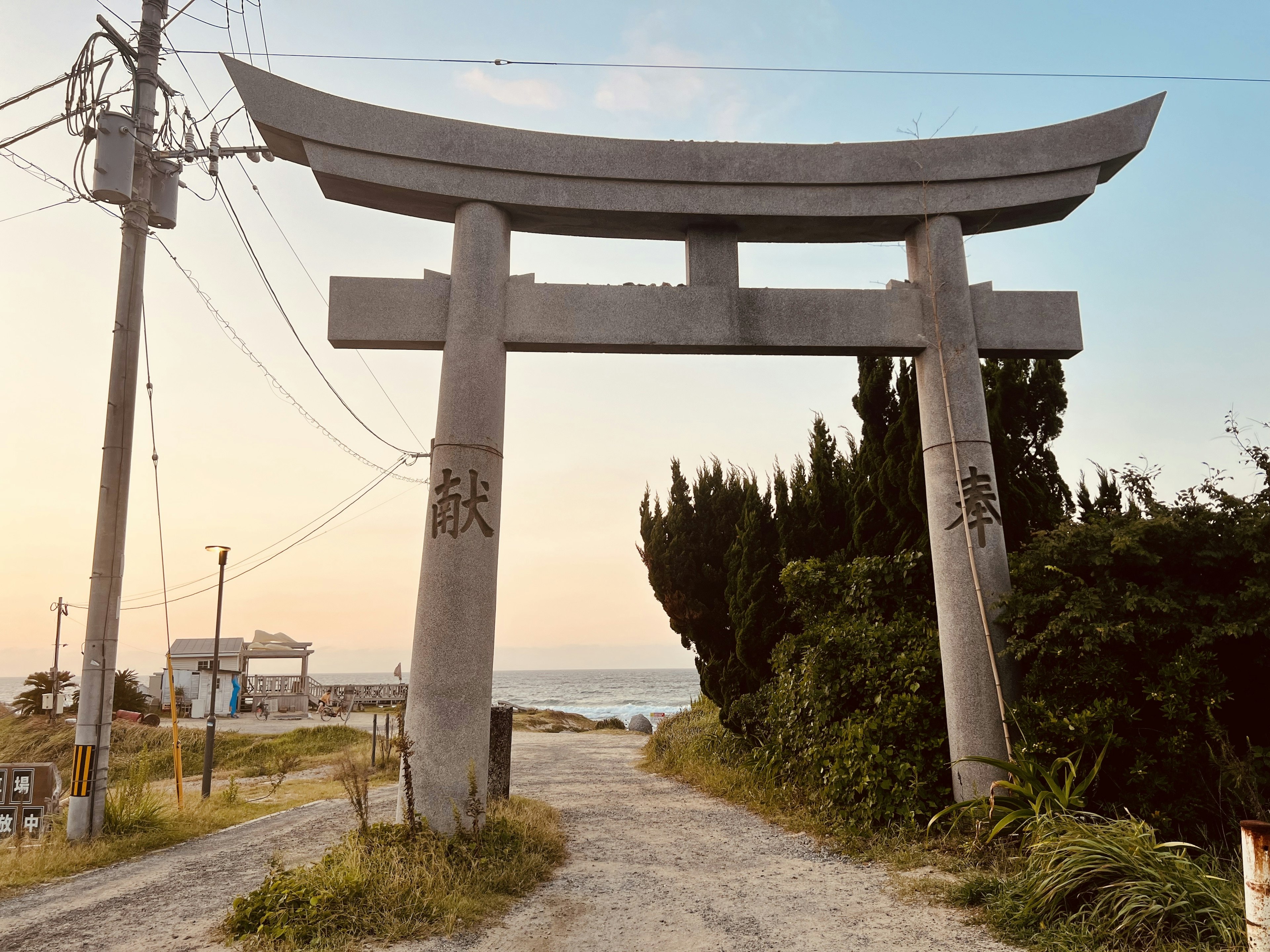 Großer Torii, der zum Meer zeigt, mit Stromleitungen im Hintergrund