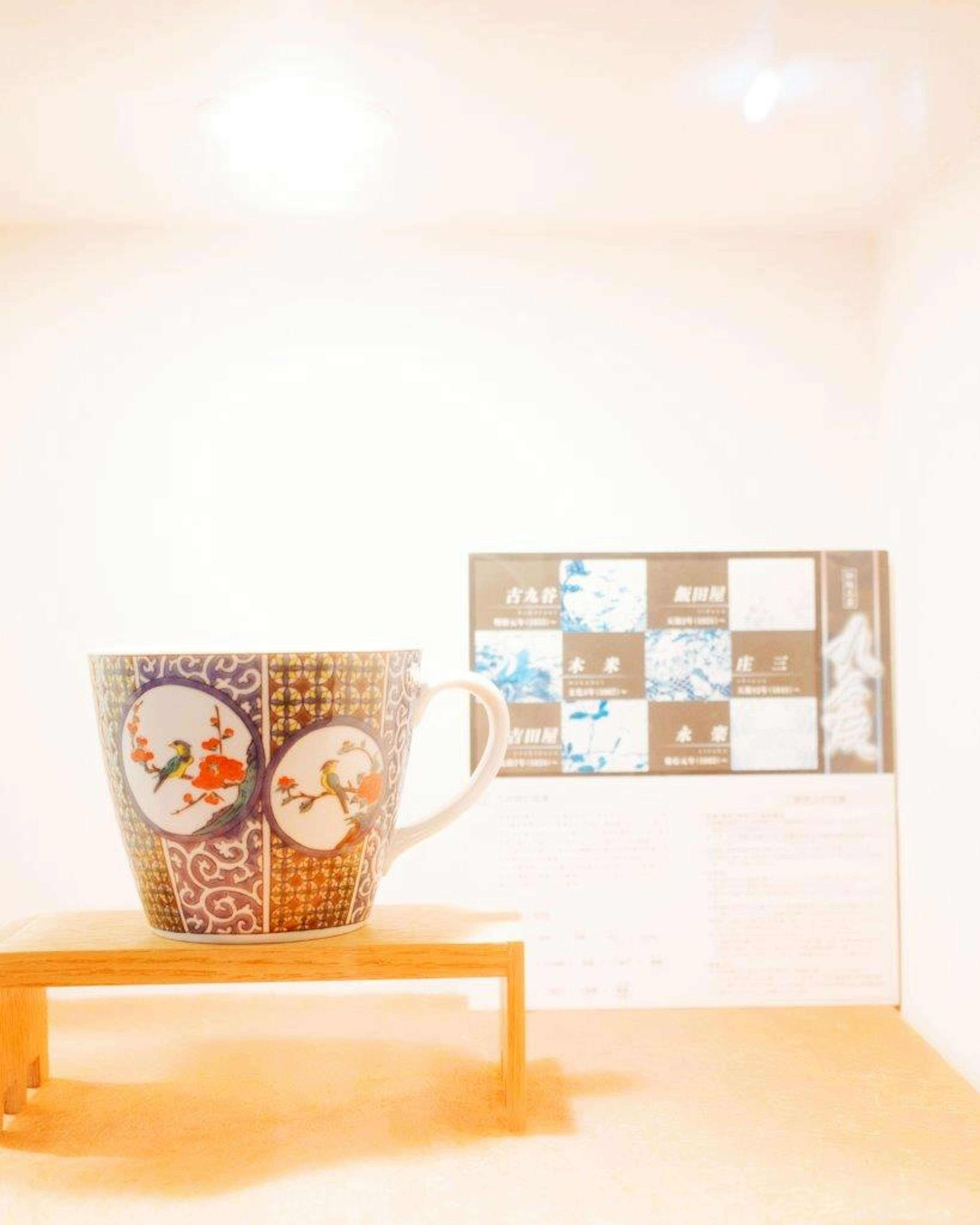 Una taza bellamente decorada colocada sobre una mesa de madera con un fondo blanco y una obra de arte detrás