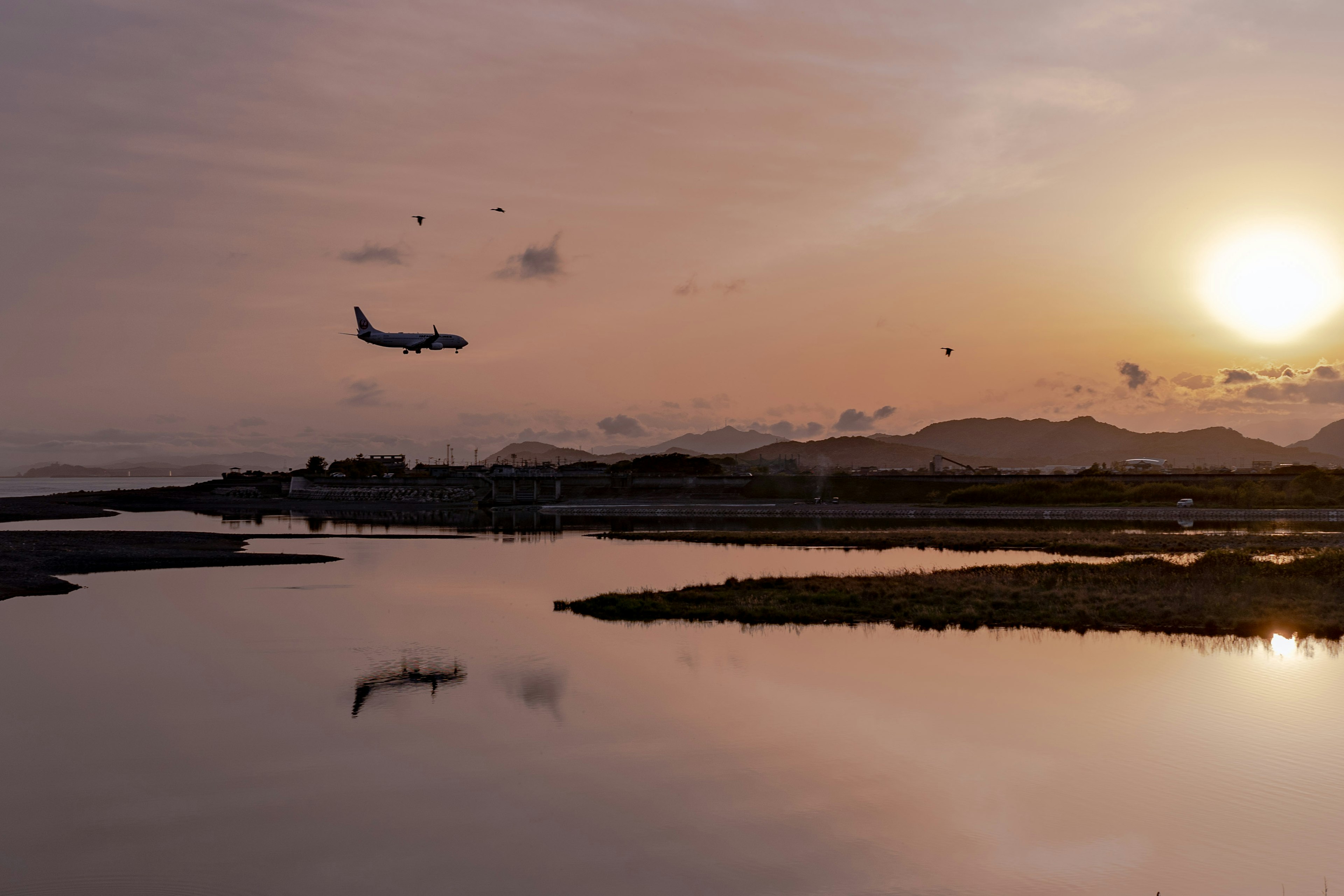 夕日を背景に飛行機が着陸するシーン川の静かな水面に映る美しい風景