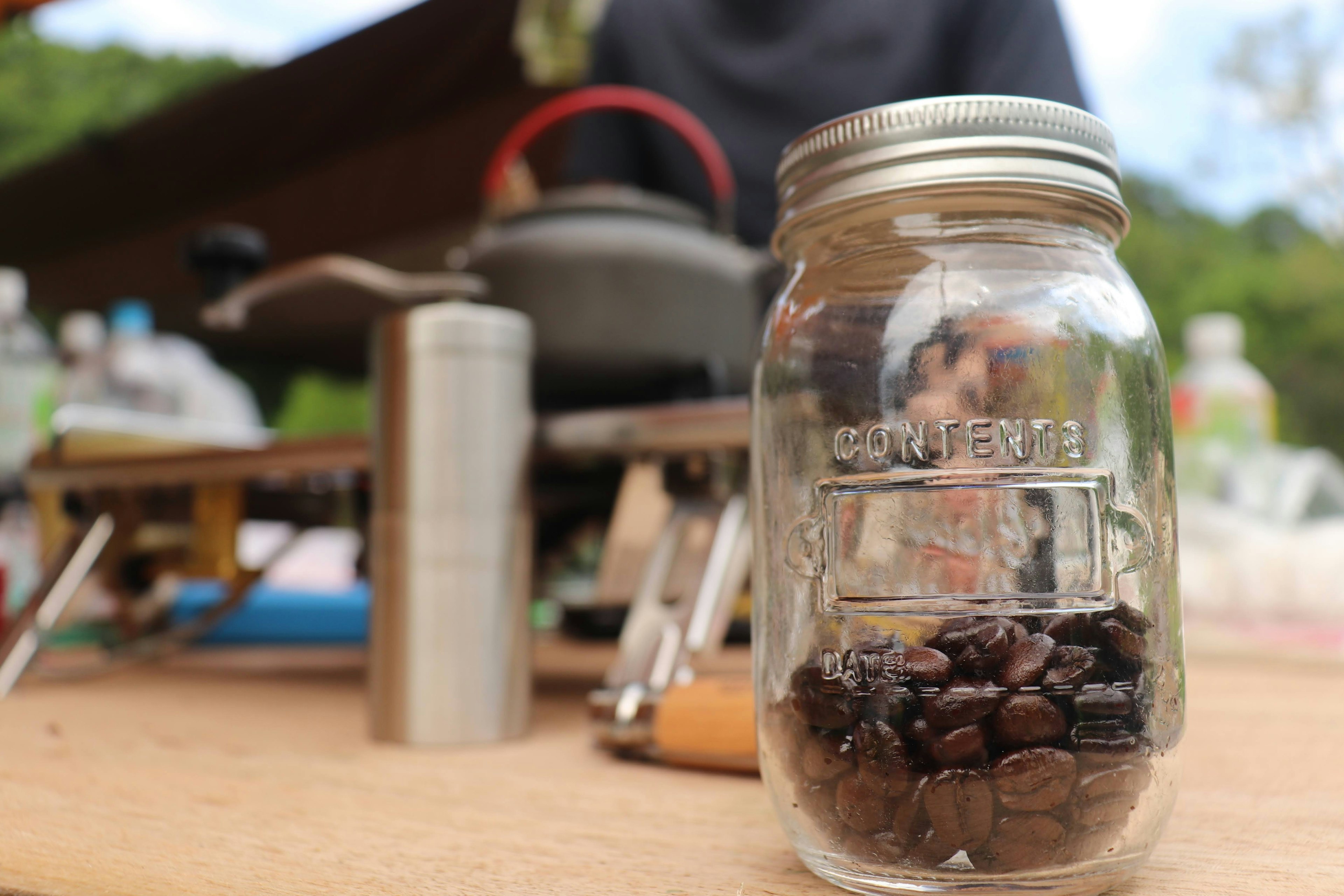 Granos de café en un frasco con un equipo de cocina al aire libre de fondo