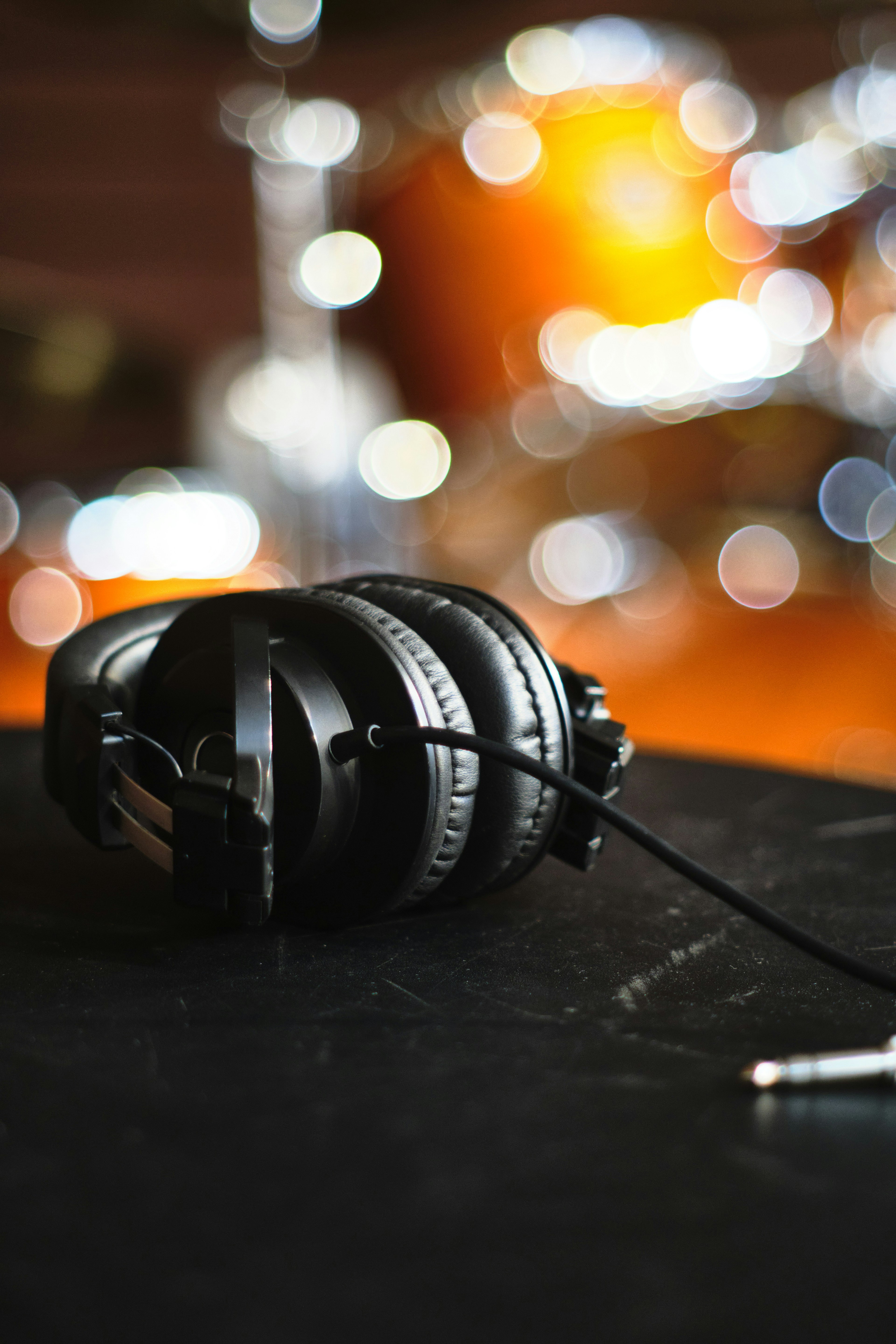 Black headphones resting on a table with a blurred drum set in the background