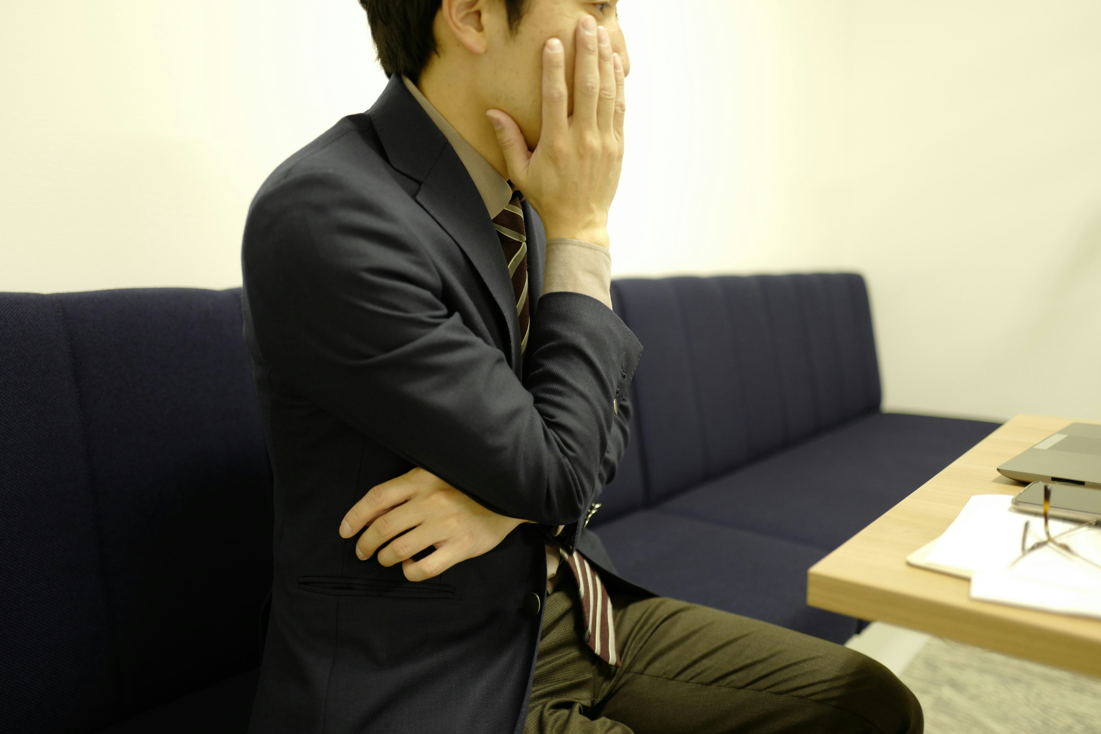 A man in a suit is deep in thought while sitting on a couch