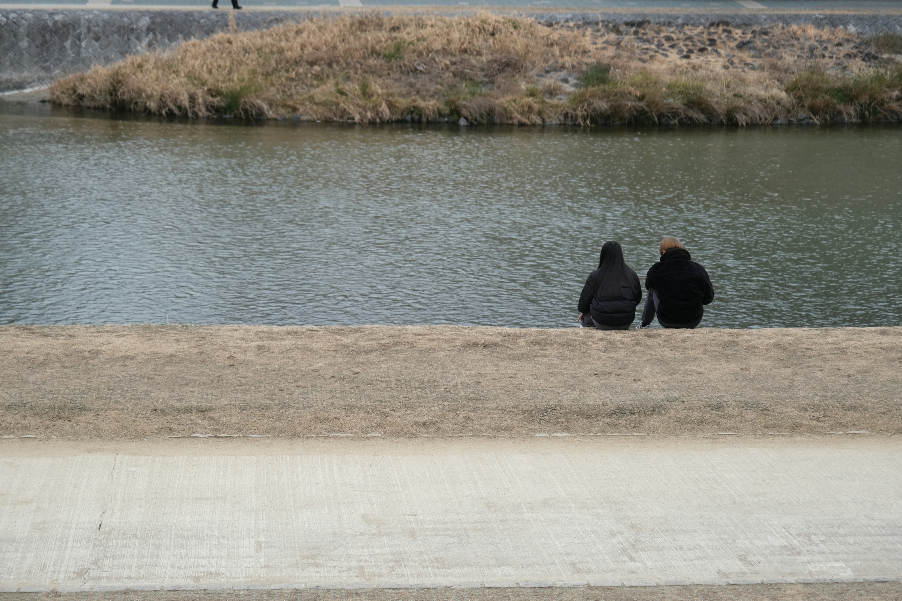 Two figures sitting by a riverbank