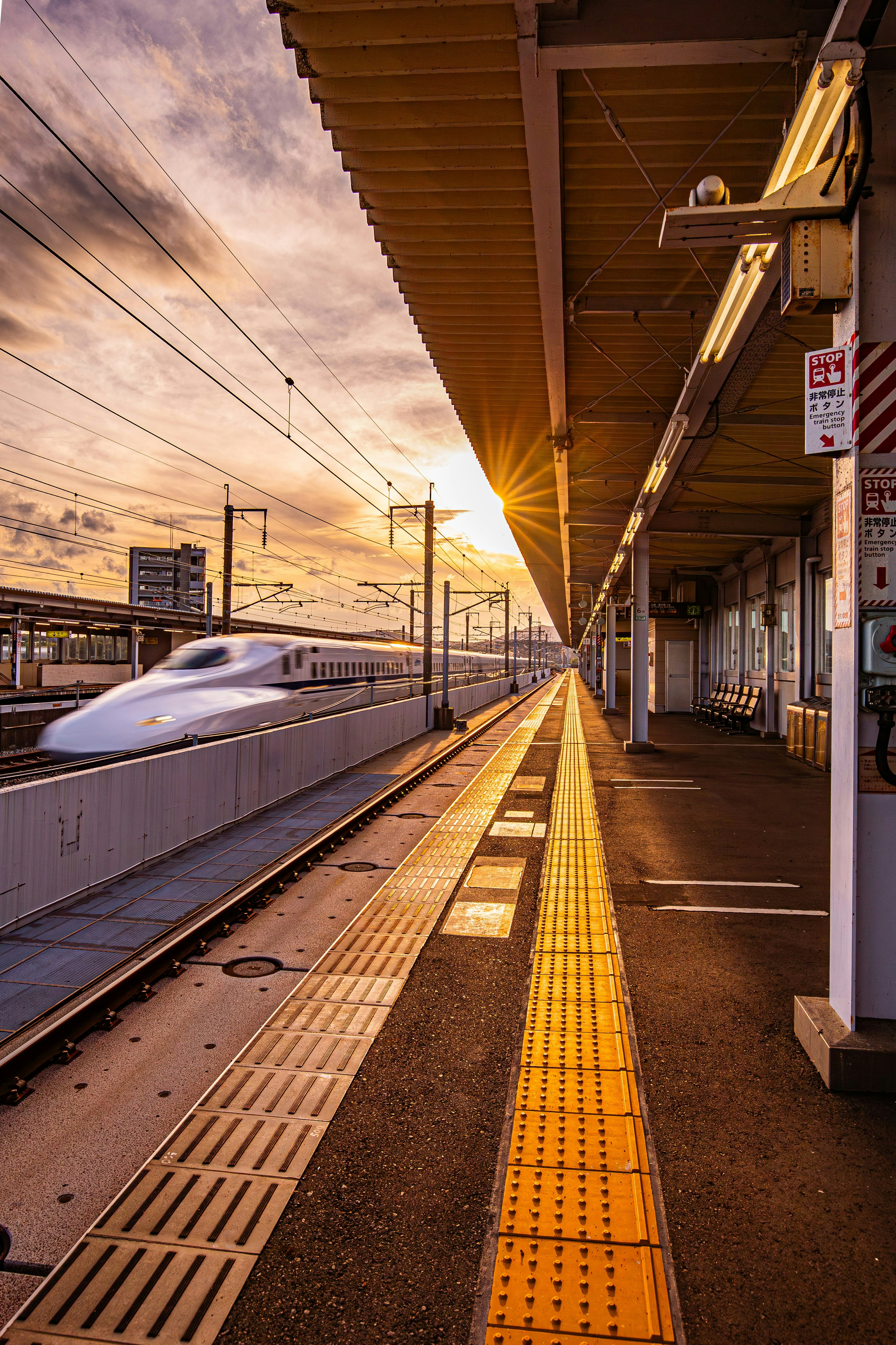 Plataforma de estación Shinkansen con un tren que se acerca al atardecer con largas vías amarillas