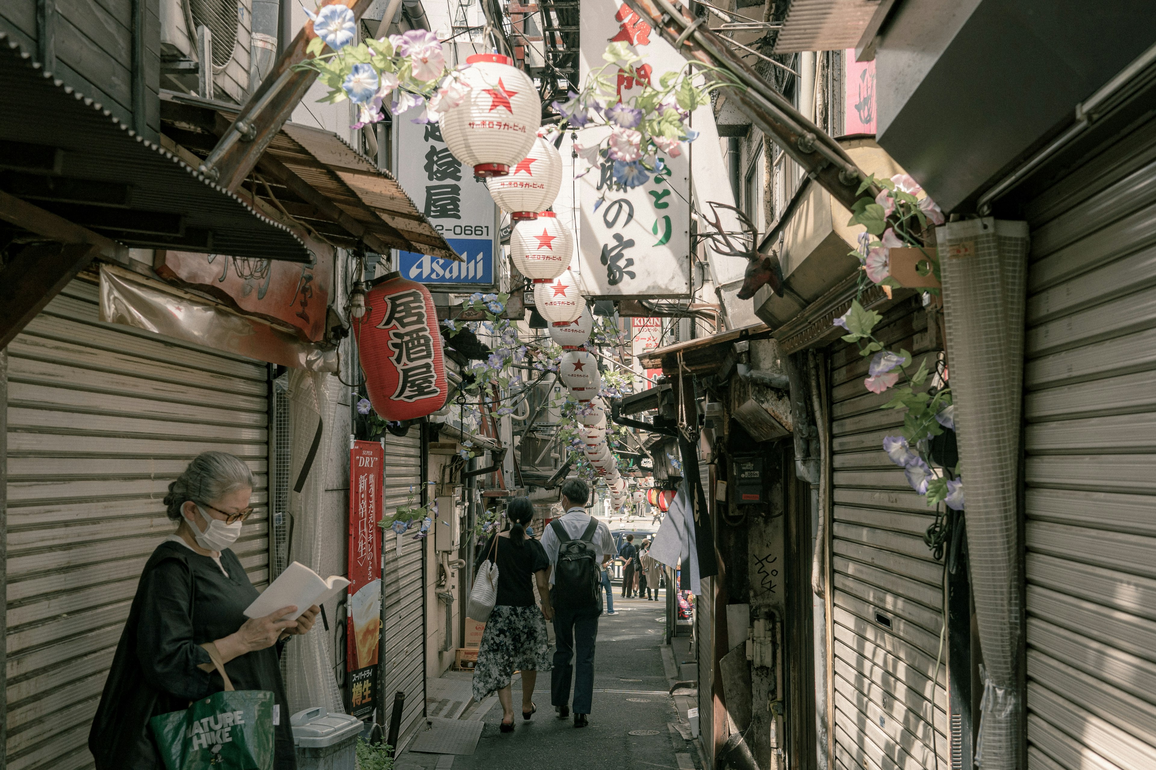 狭い路地に並ぶ提灯と店舗のシャッターを背景に歩く人々