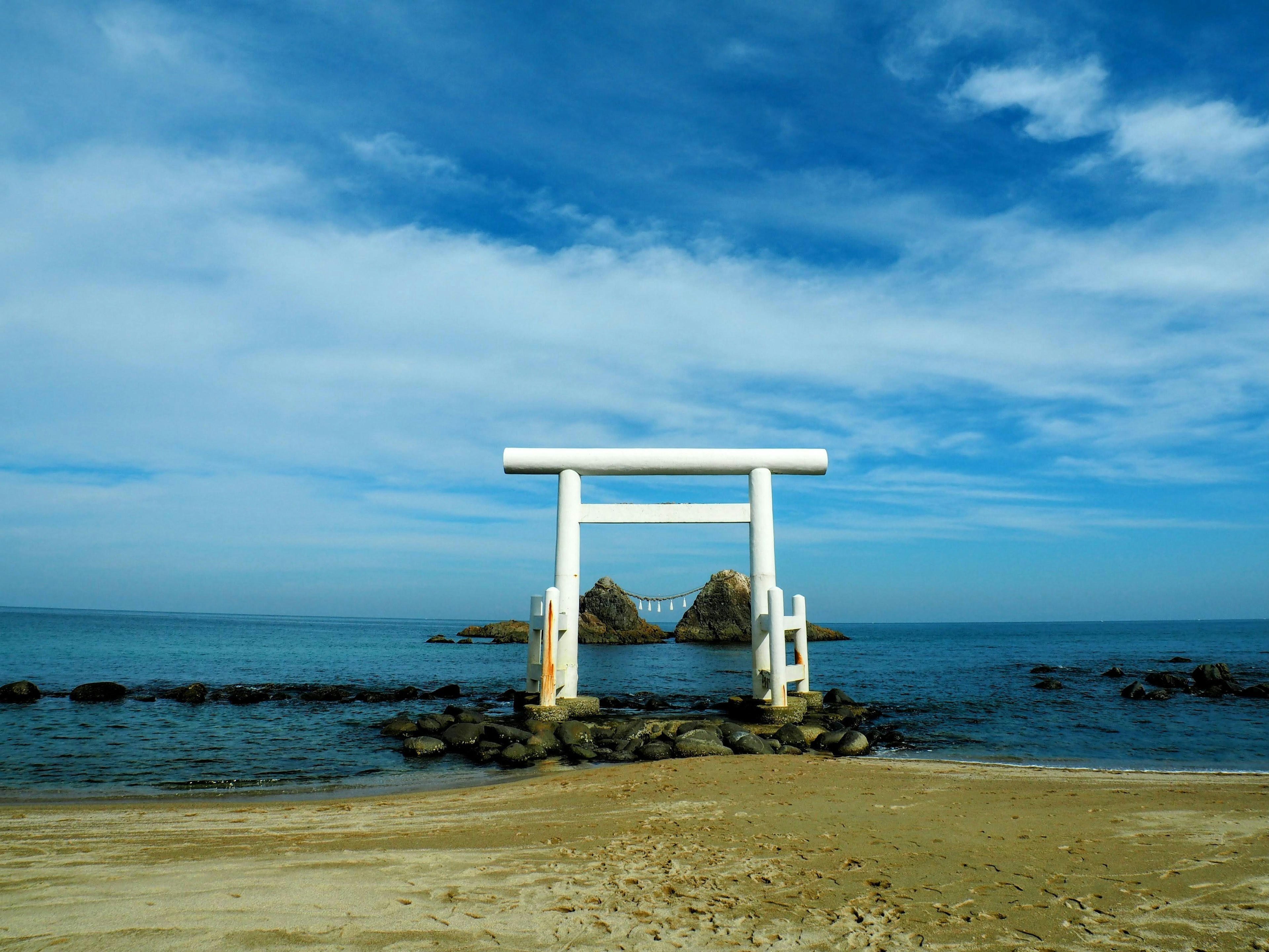 Puerta torii blanca con vista al mar bajo un cielo azul