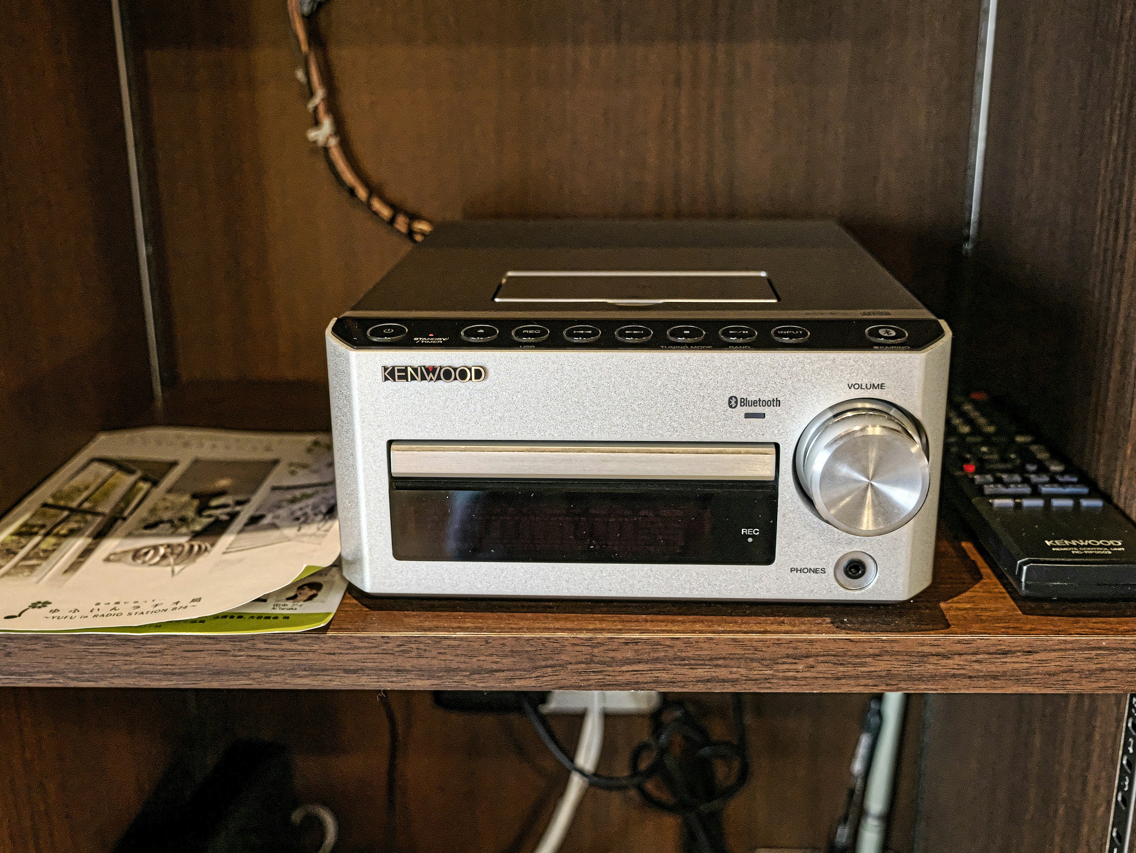 Compact audio system on a wooden shelf with a remote control and music player