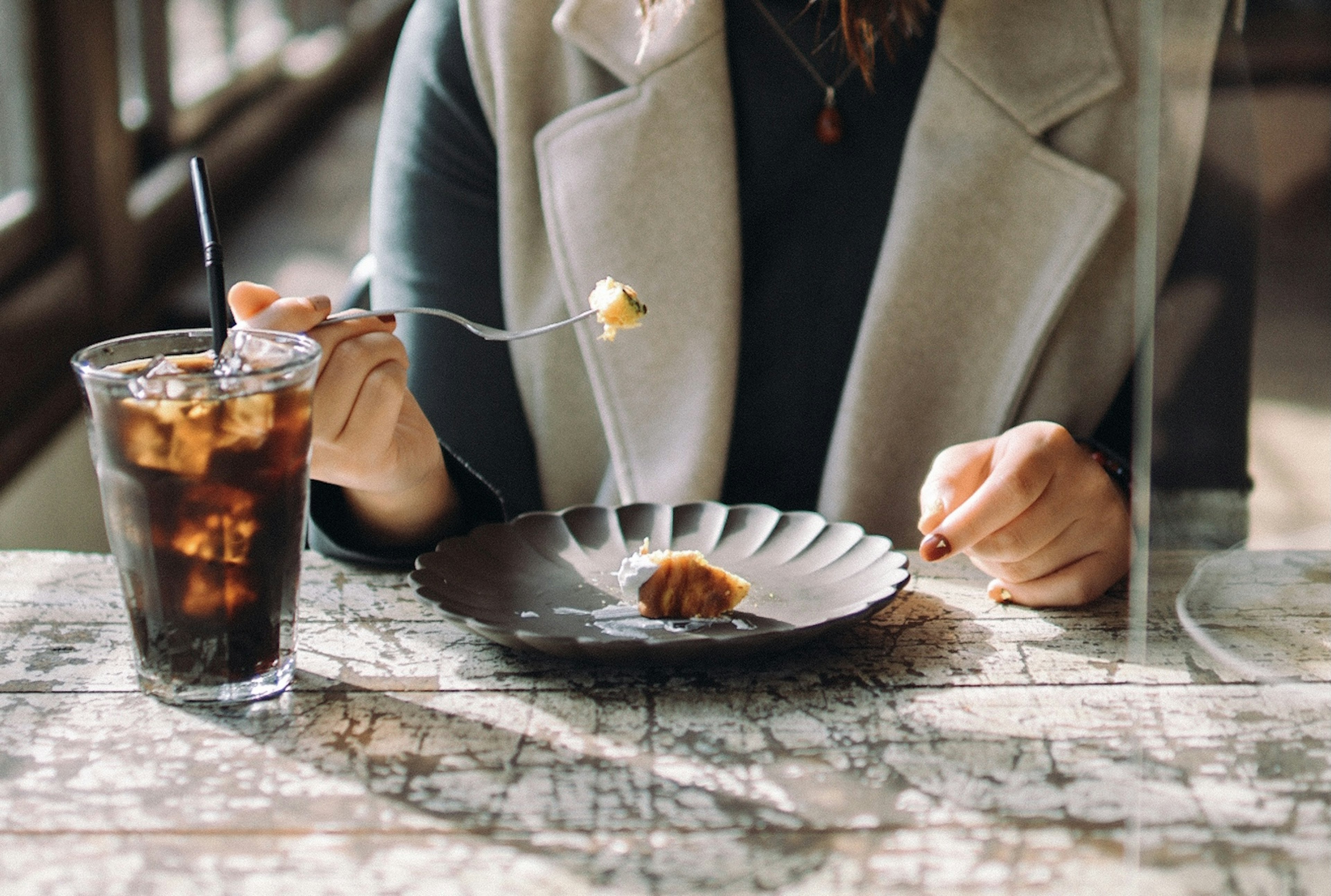 女性在桌子上吃甜点时手握甜点叉子和饮料