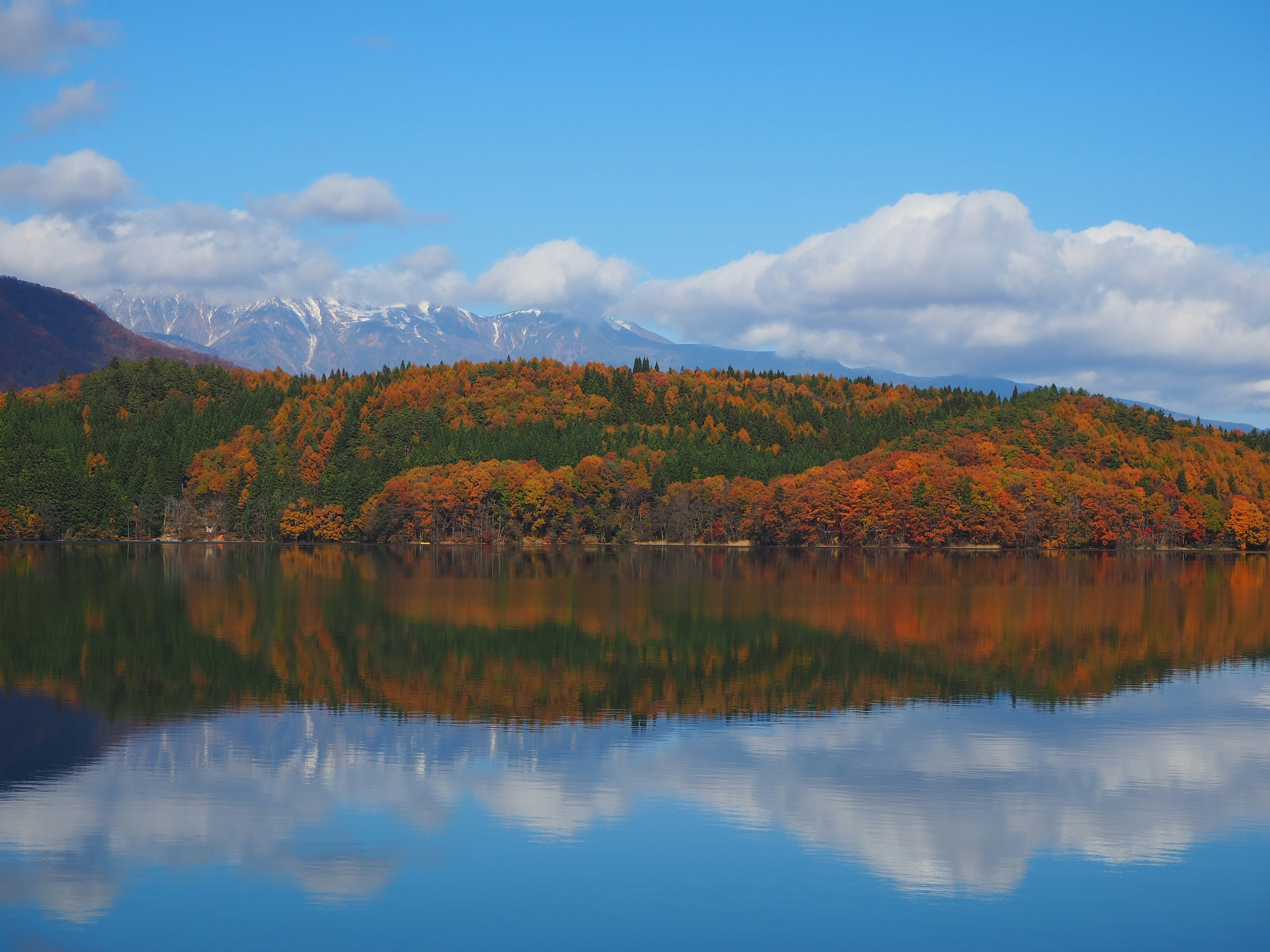 Paysage d'automne pittoresque reflété dans un lac calme feuillage vert et orange vibrant sur les collines sous un ciel bleu clair