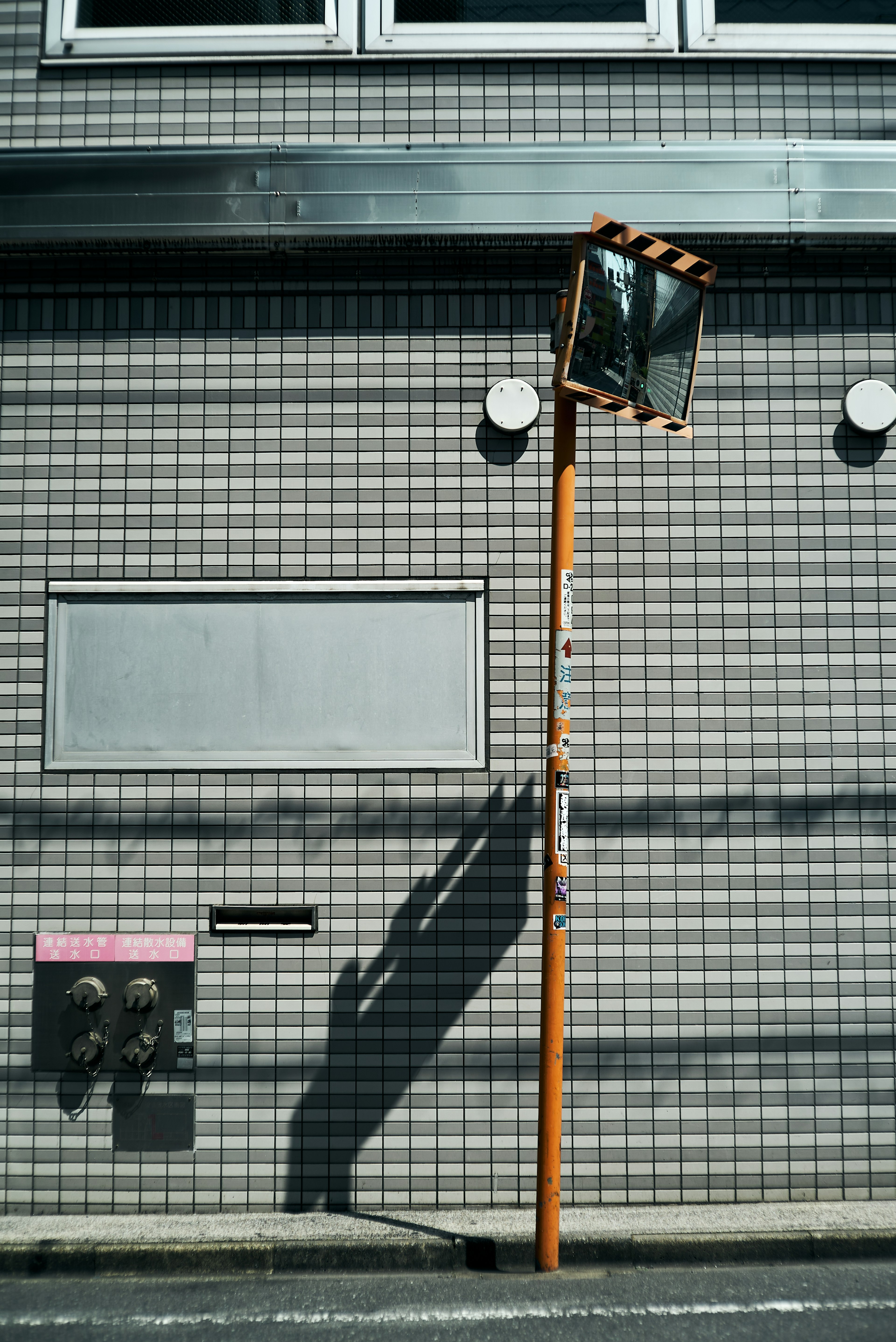 Oranger Pfosten mit einem Spiegel, der einen Schatten an eine geflieste Wand wirft