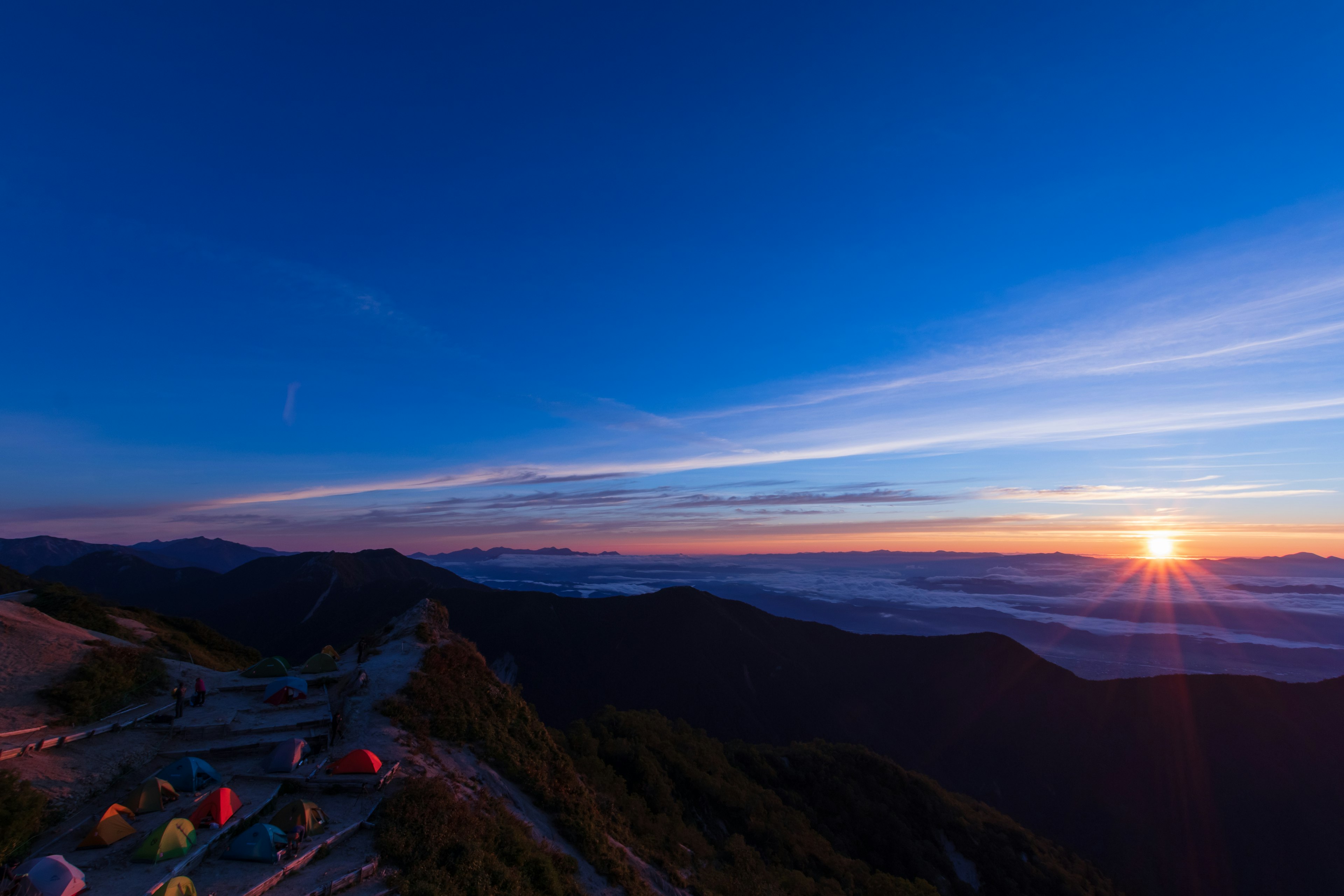 Vista panoramica delle montagne all'alba con tende colorate in primo piano