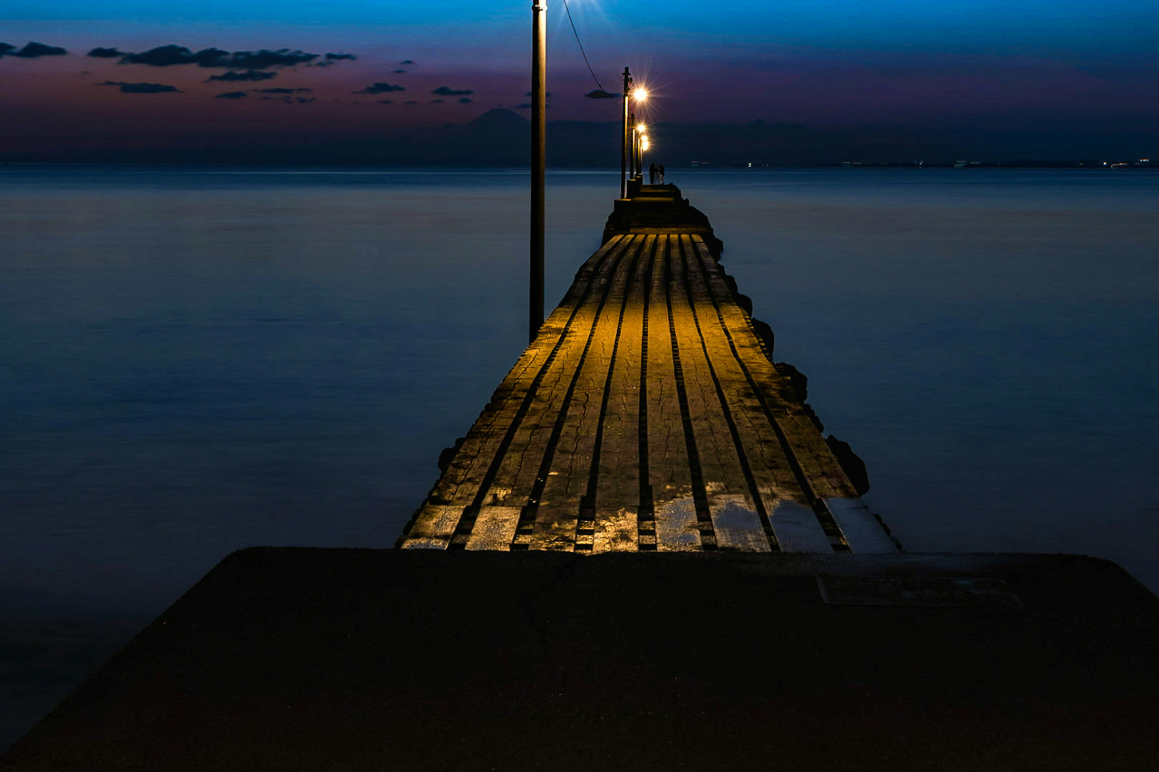 Vista notturna di un molo in legno che si estende nell'acqua calma illuminato da luci