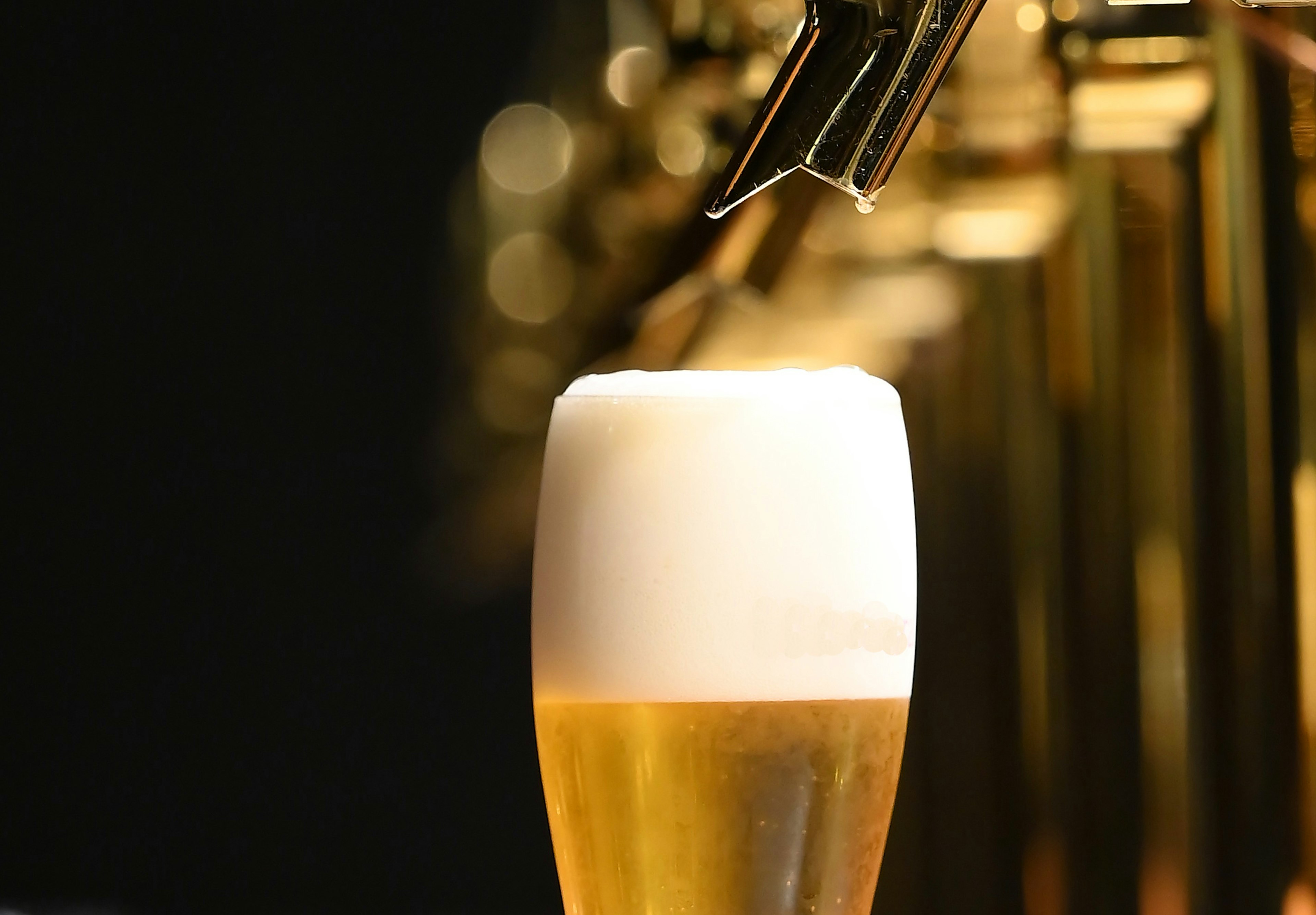 Vaso de cerveza con espuma y grifo de cerveza al fondo