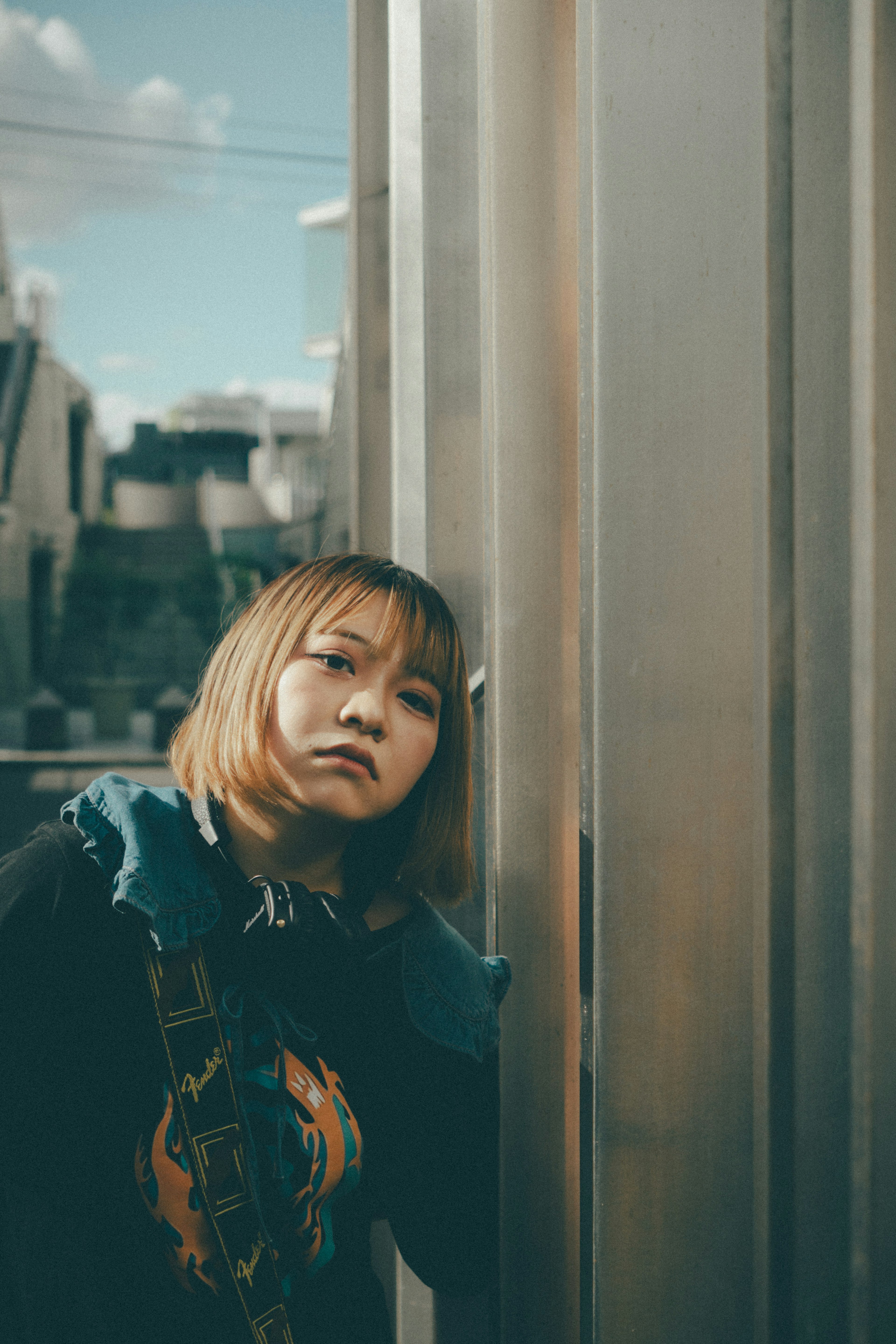 A young woman with blonde hair leaning against a metal pillar in an urban setting