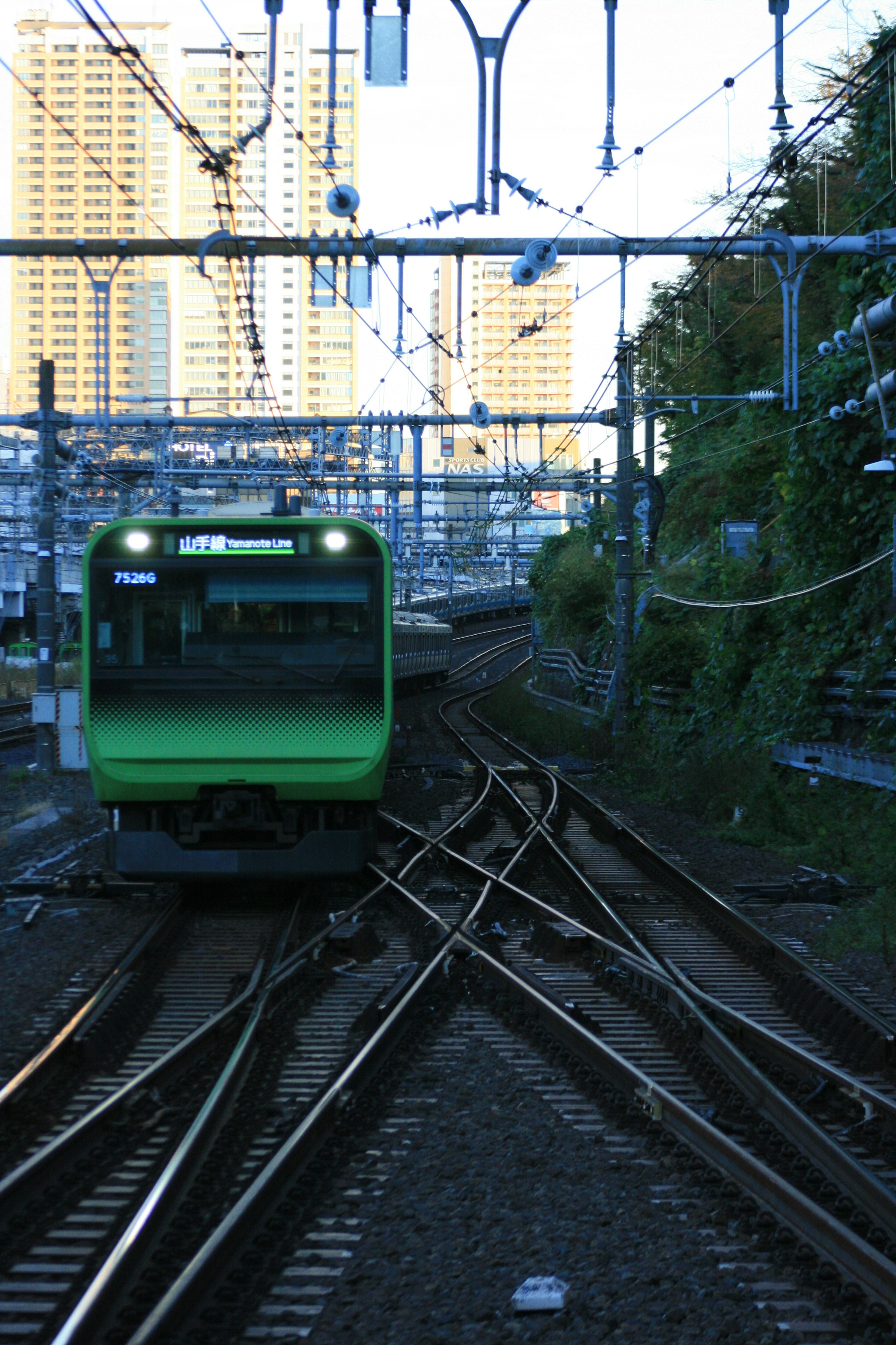 Green train on diverging railway tracks with skyscrapers in the background