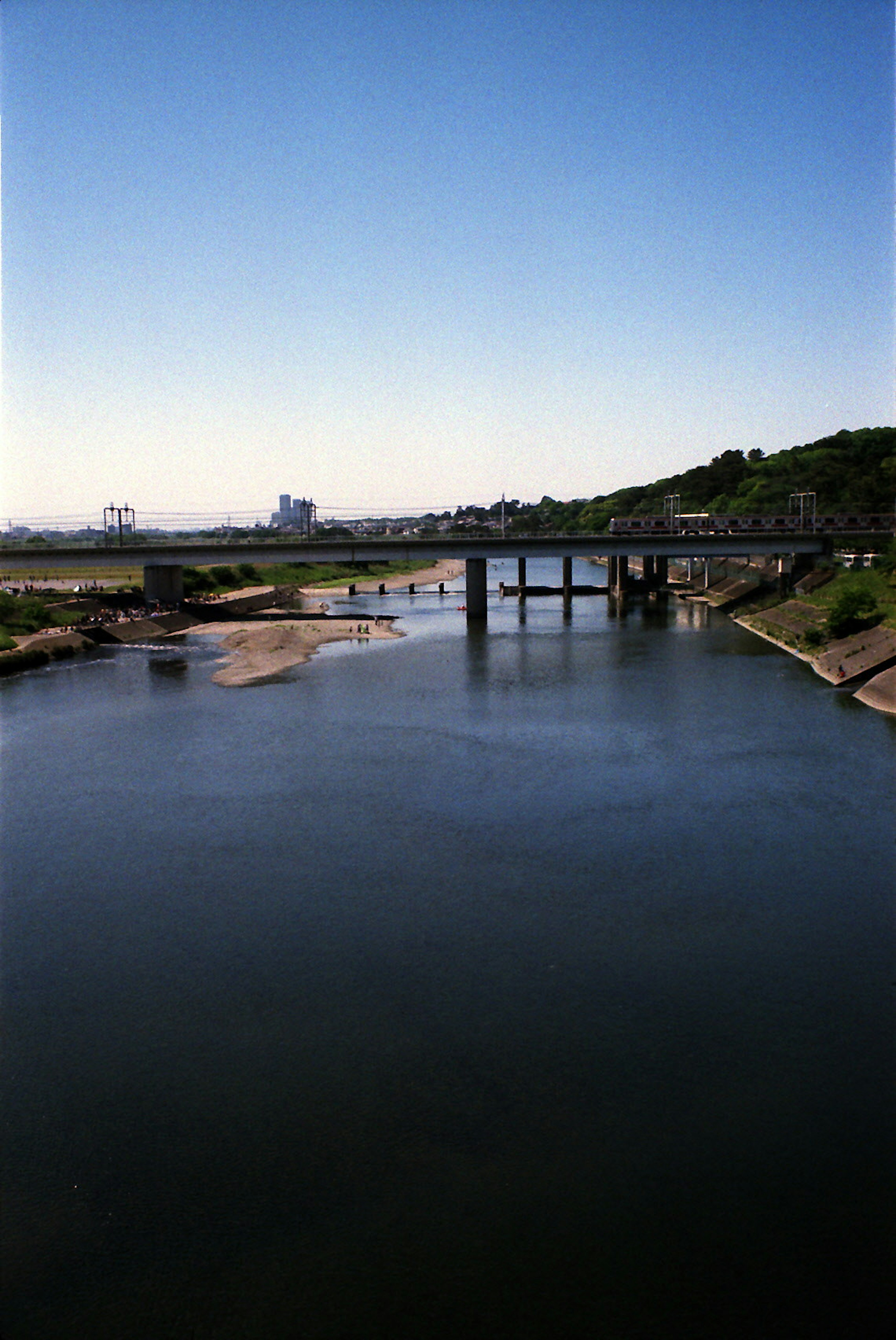 Vista escénica del río con cielo azul y agua tranquila puente que cruza el río rodeado de colinas verdes