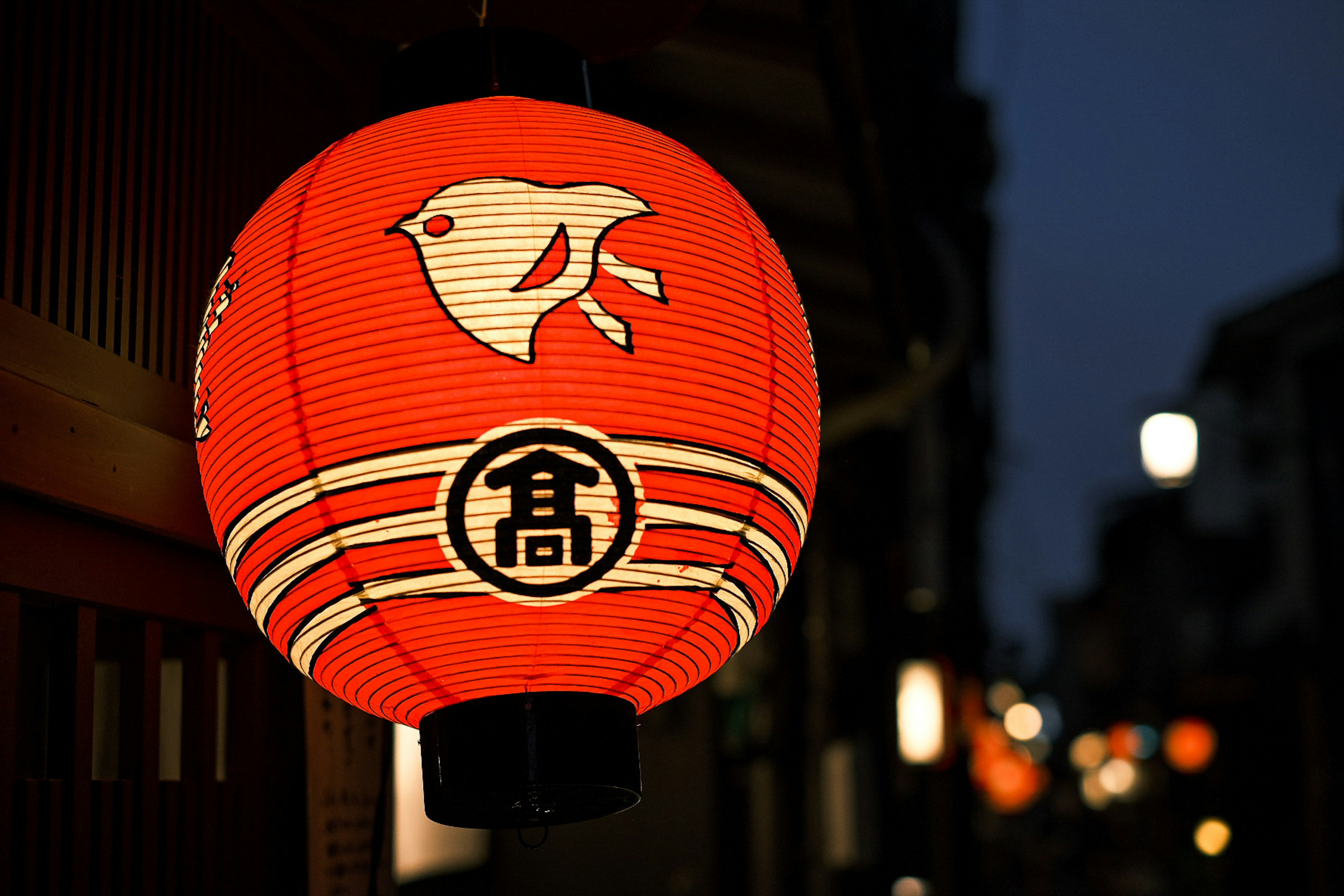 Farol rojo con diseño de pájaro blanco y logo kanji en un entorno nocturno