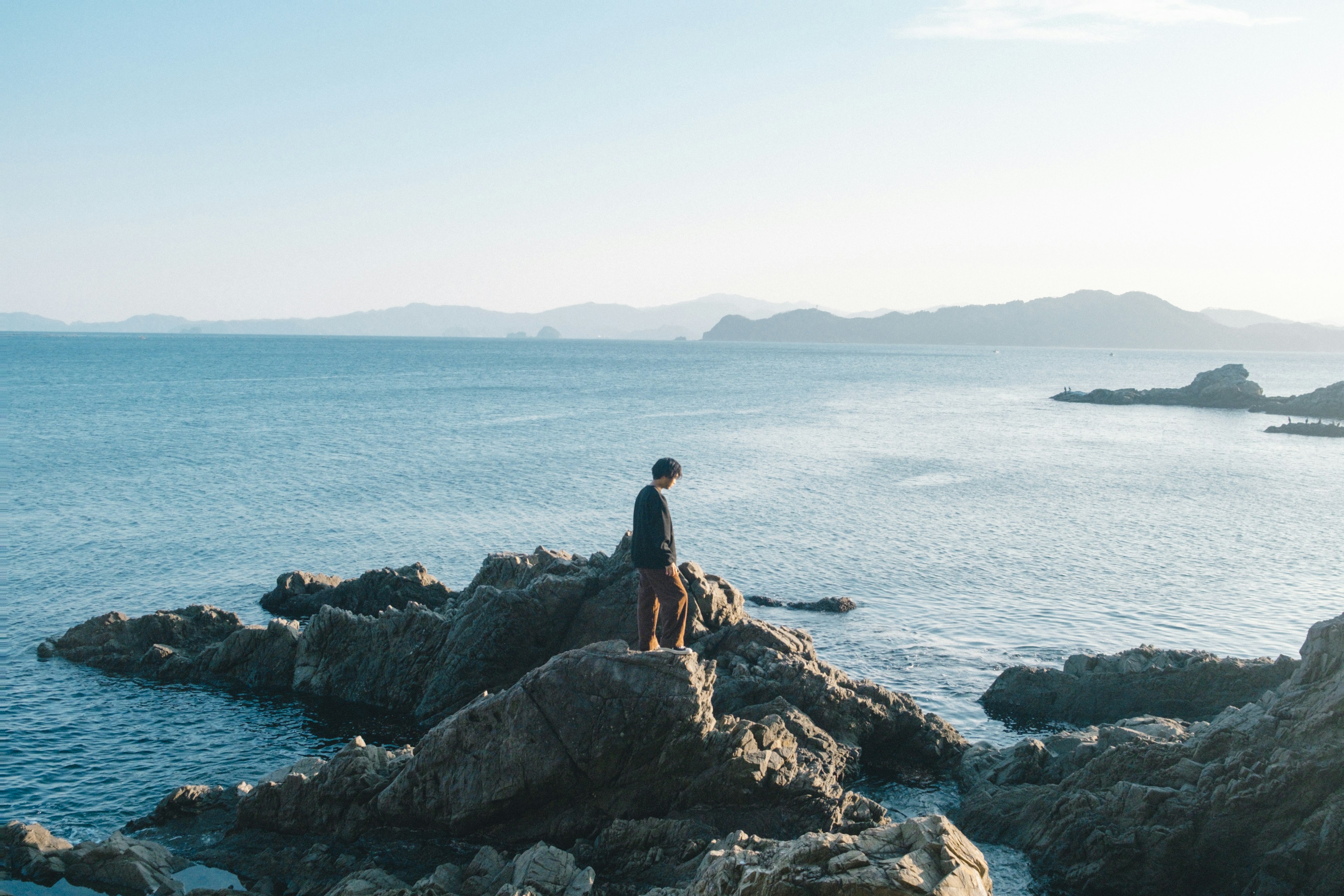 Silhouette d'un homme se tenant sur une côte rocheuse avec une mer calme en arrière-plan