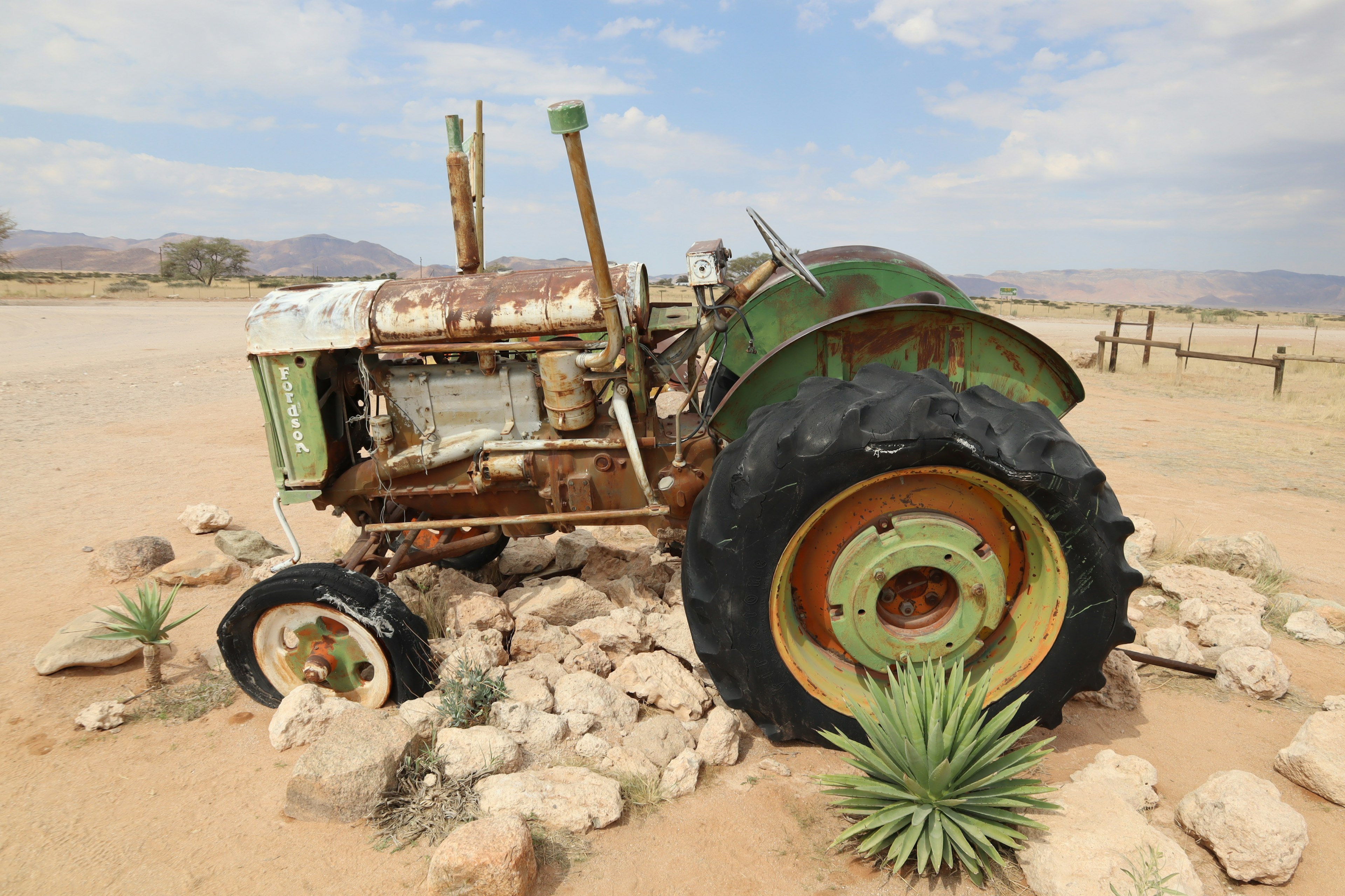 Old green tractor surrounded by cacti and rocks