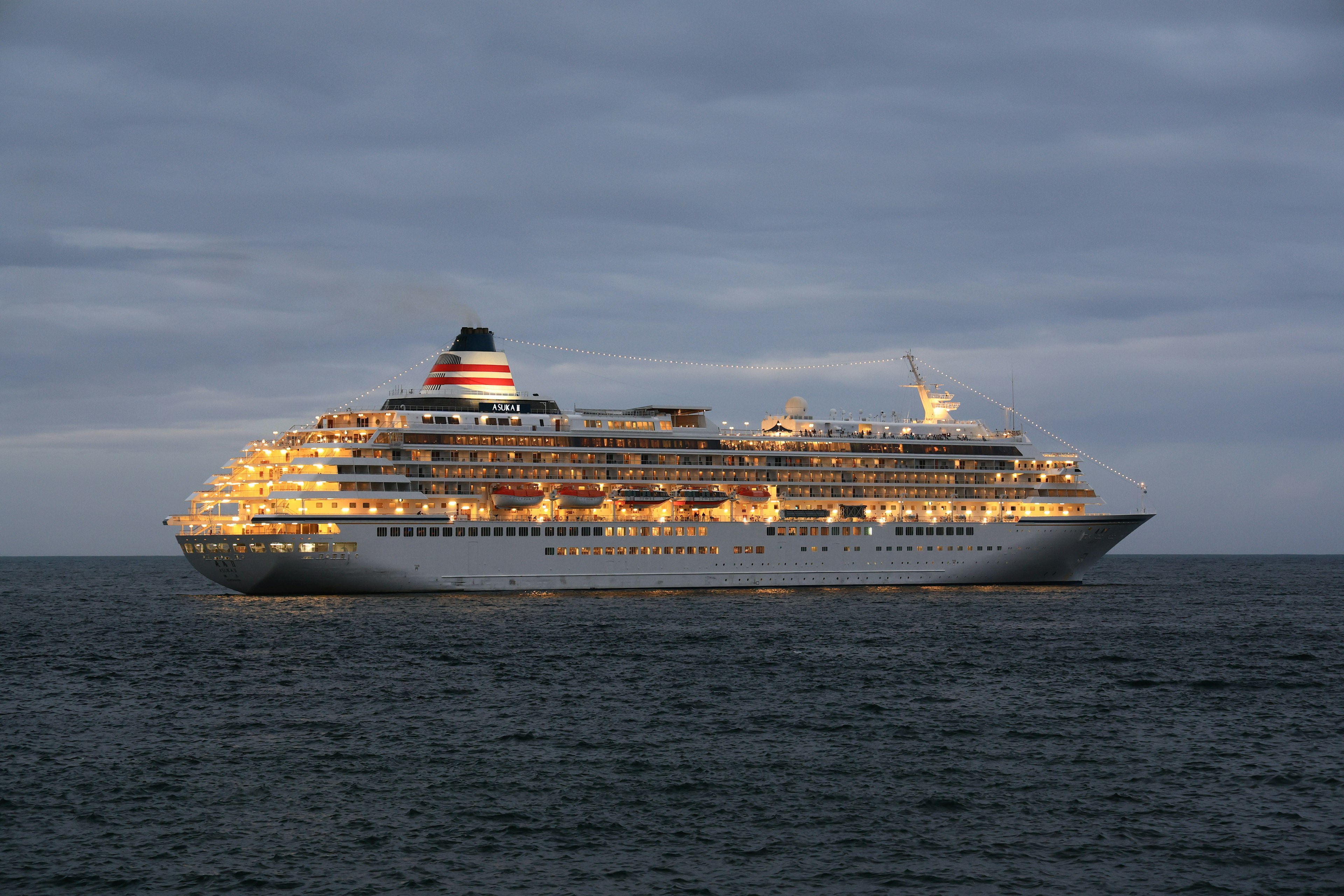 Luxus-Kreuzfahrtschiff, das auf dem Ozean schwimmt Helle Lichter beleuchten das Schiff unter einem bewölkten Himmel