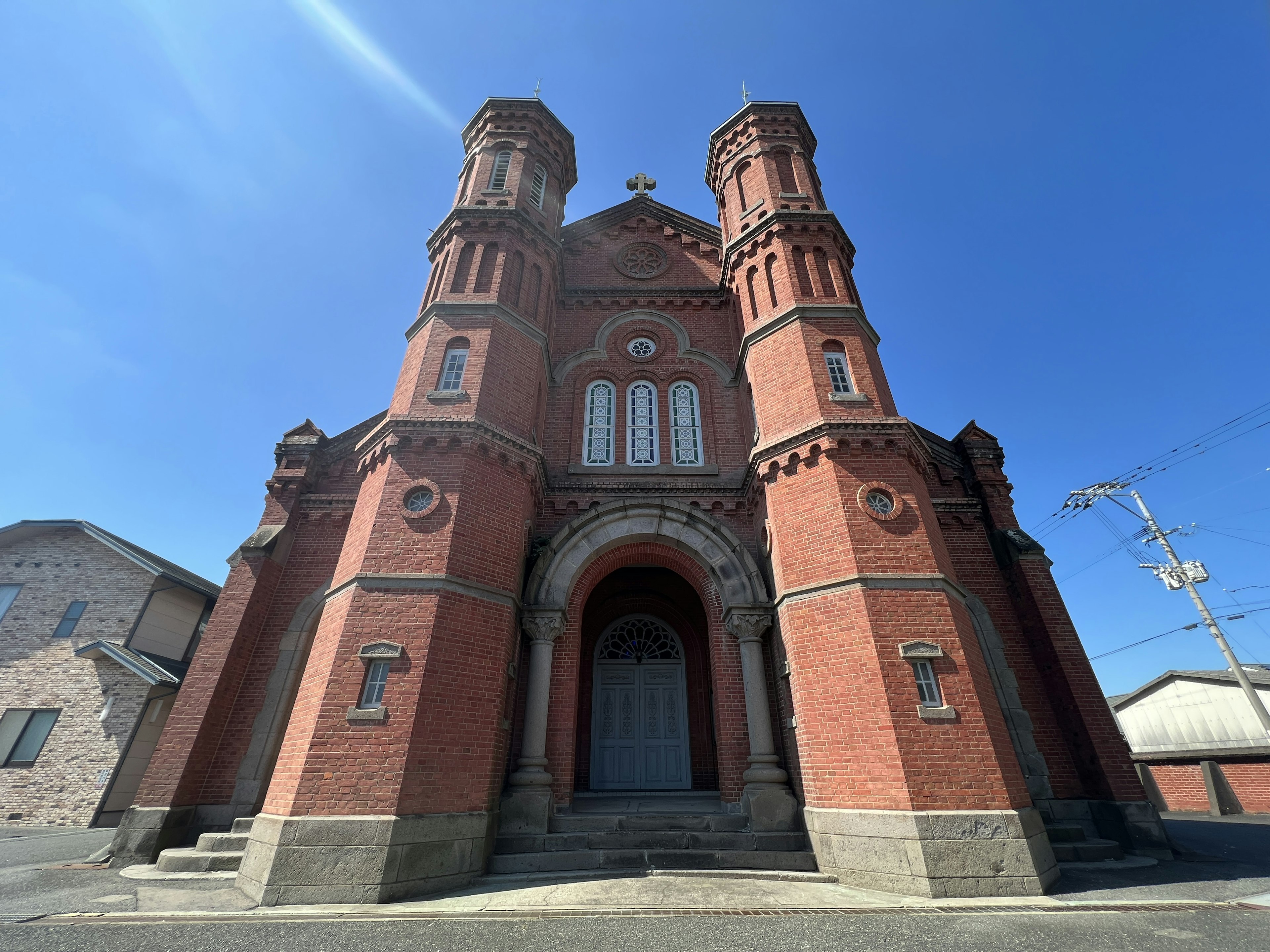 Red brick church exterior with tall towers under a bright blue sky