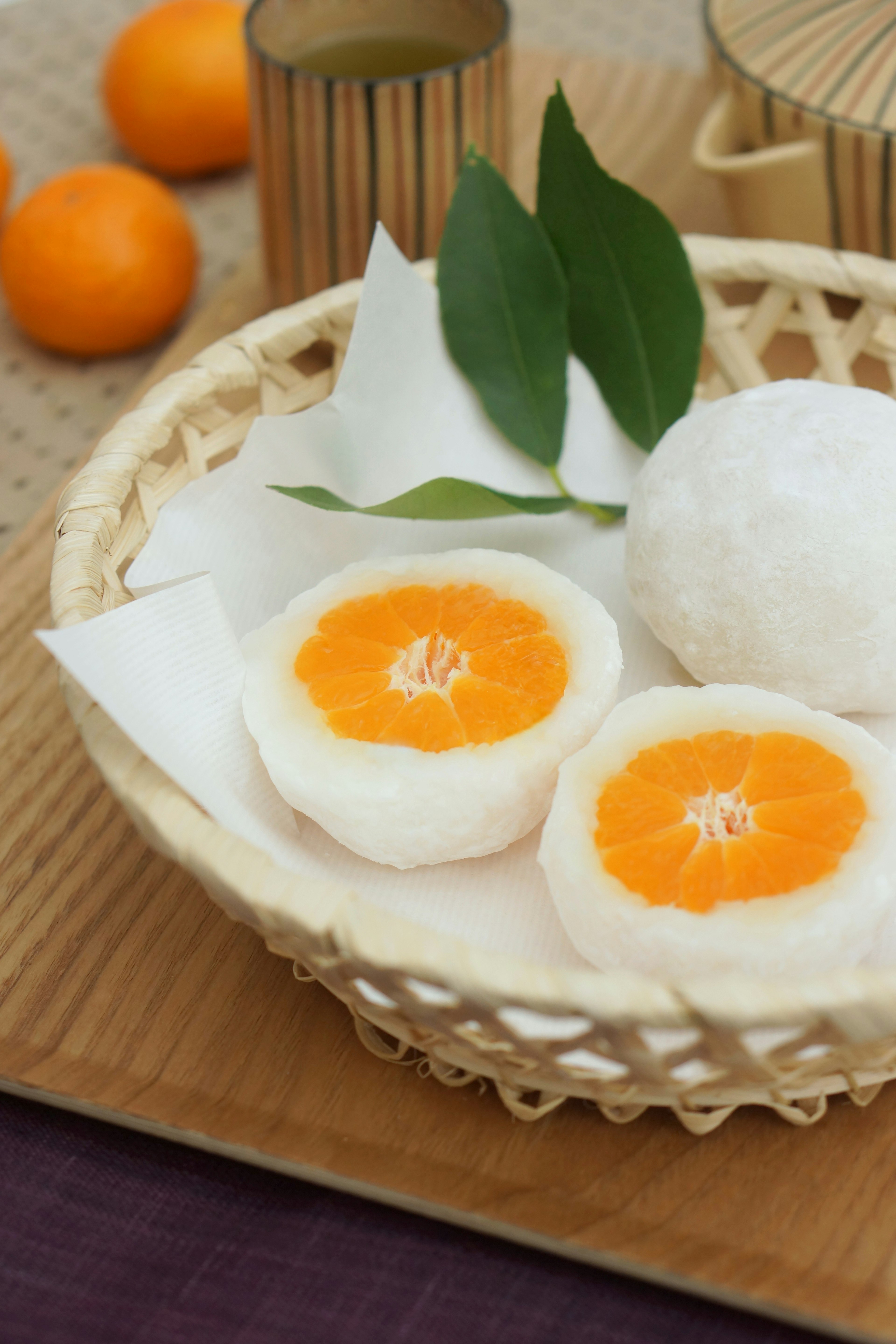 Una cesta de bambú llena de mochi y rodajas de naranja decoradas con hojas