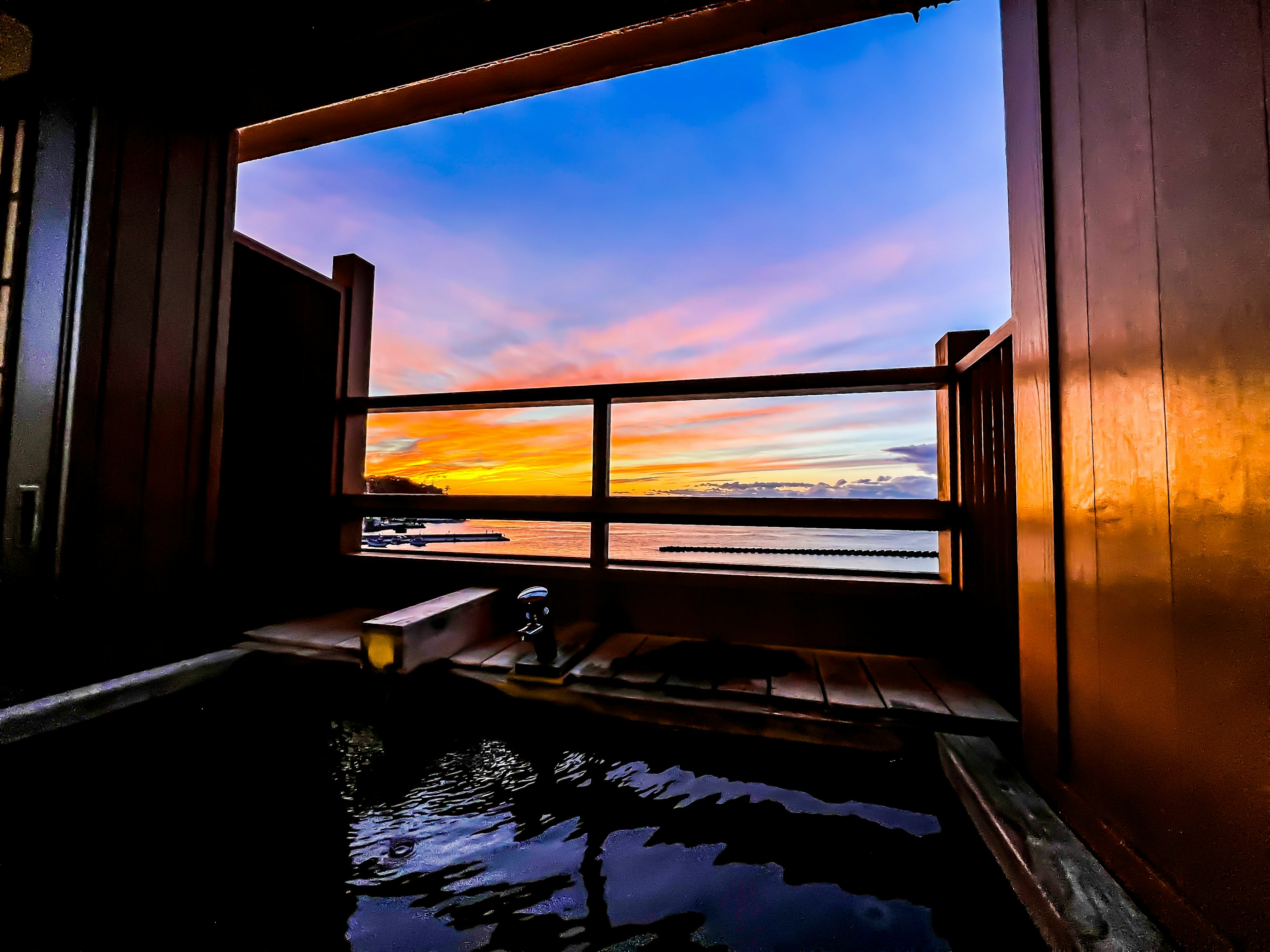 Scenic view of an outdoor hot spring at sunset with colorful sky reflections on the water