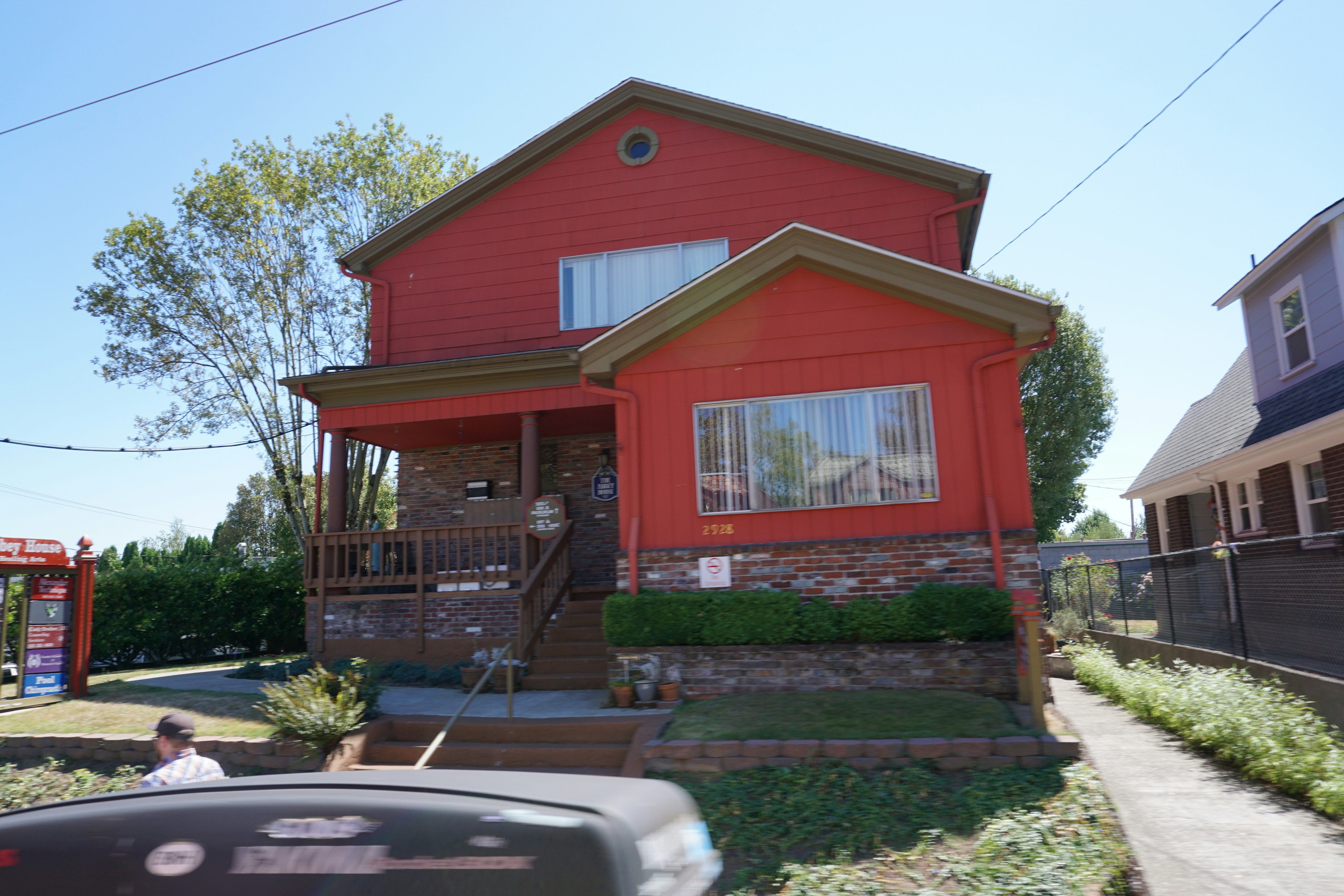 Maison à deux étages avec une façade rouge, grandes fenêtres et jardin visible