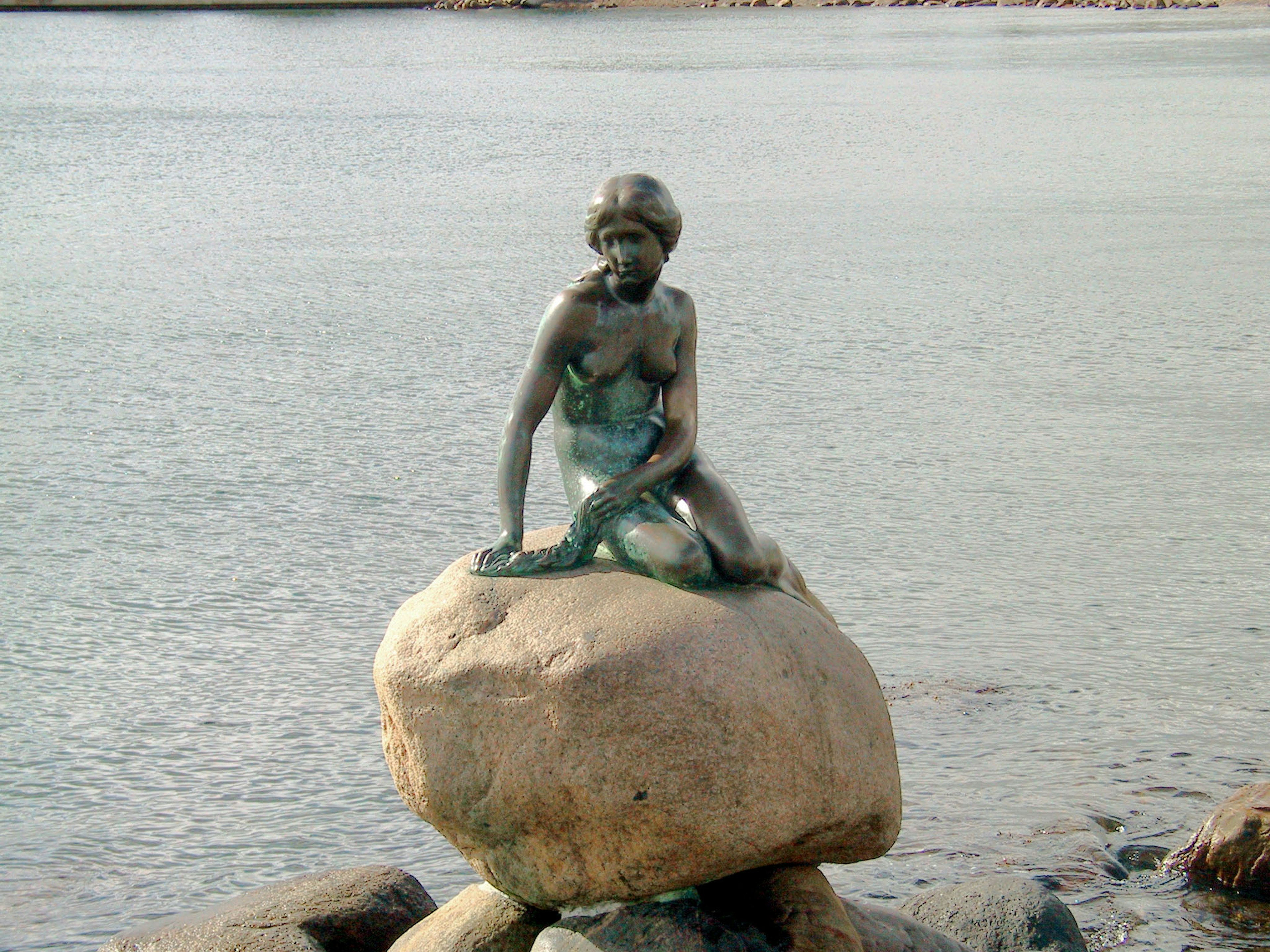 Statue de sirène assise sur un rocher au bord de la mer