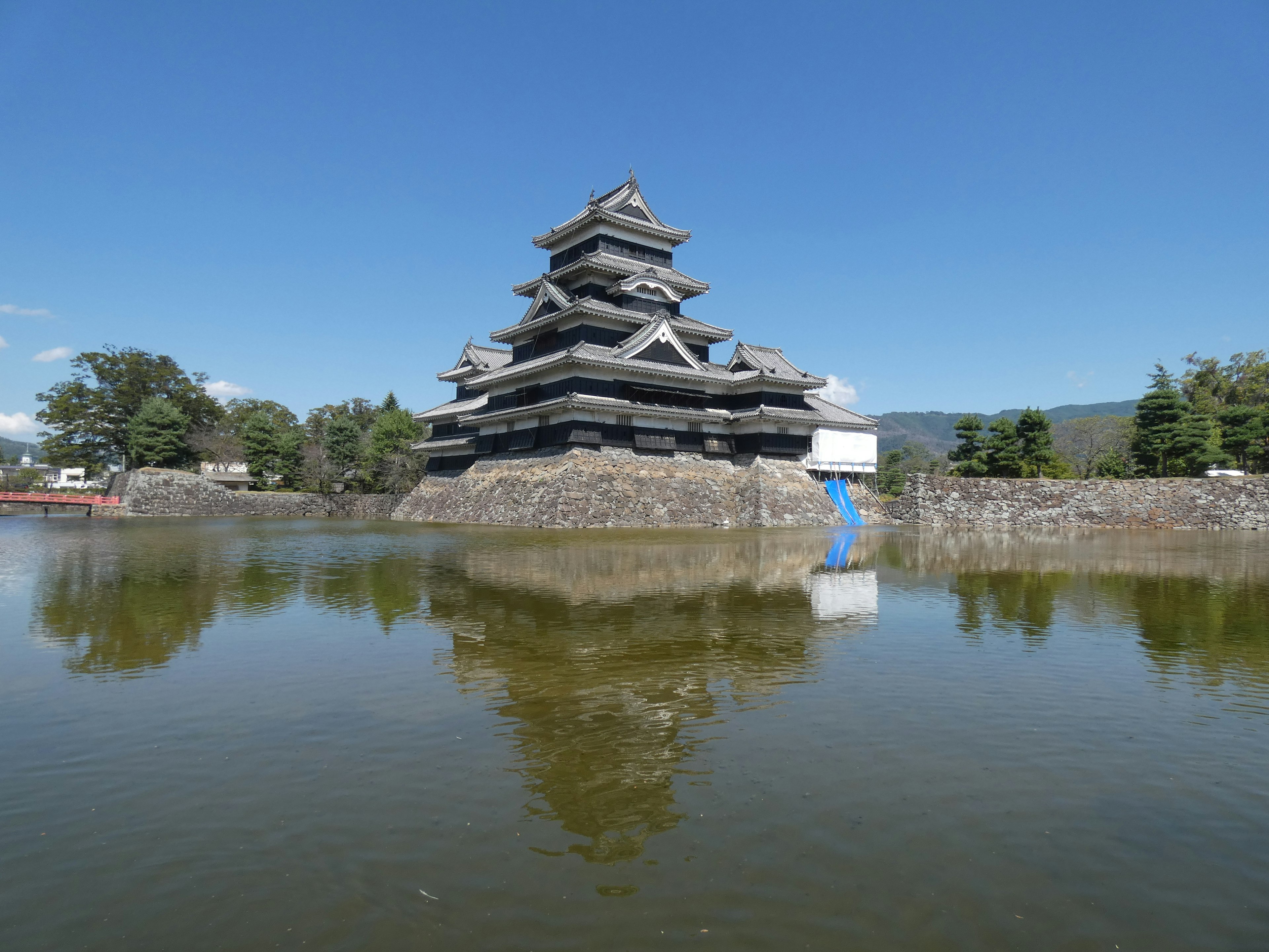 Die beeindruckende Außenansicht von Matsumoto Castle spiegelt sich im Wasser unter einem klaren blauen Himmel