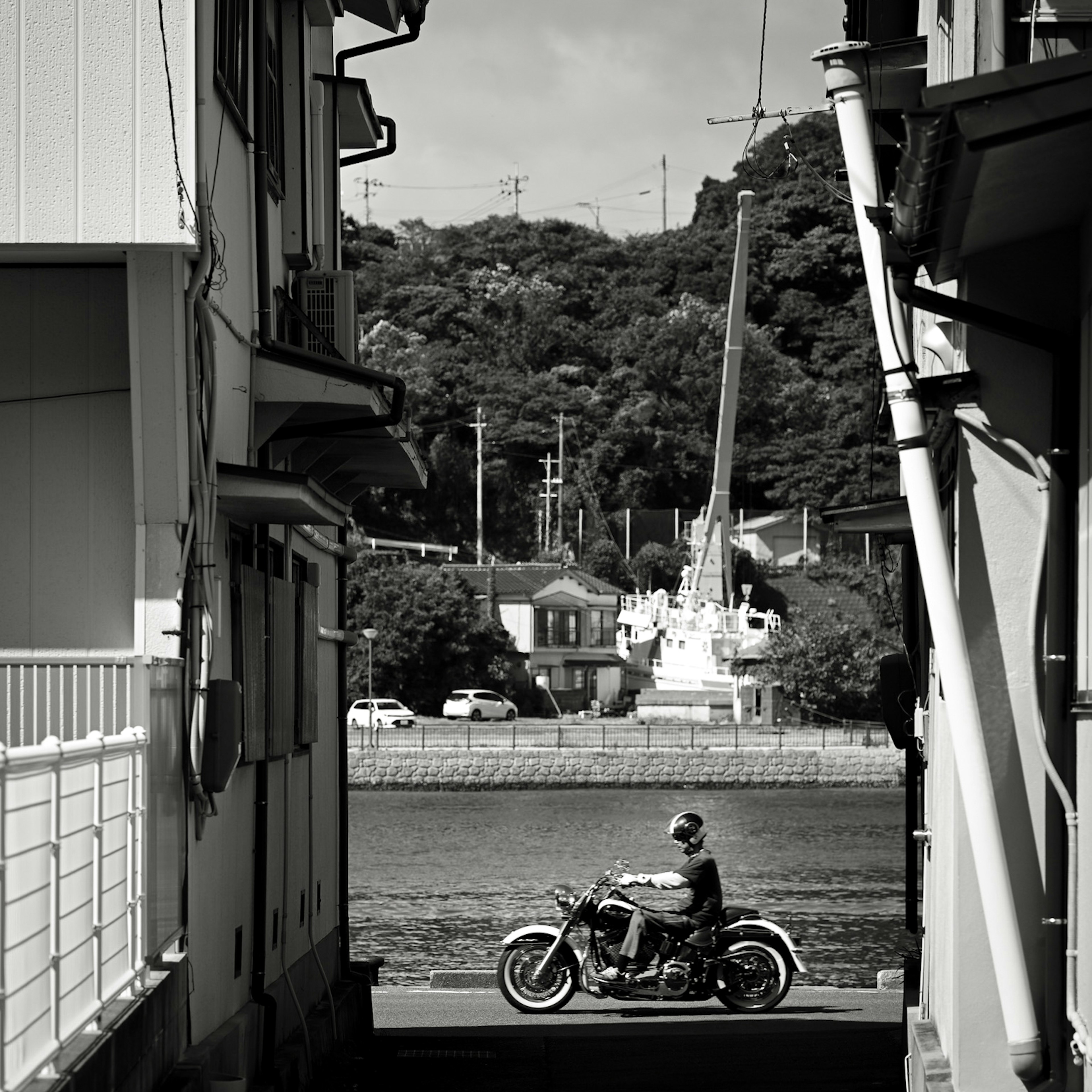 黒と白のストリートシーンでバイクに乗る人物が見える背景には山と建物がある