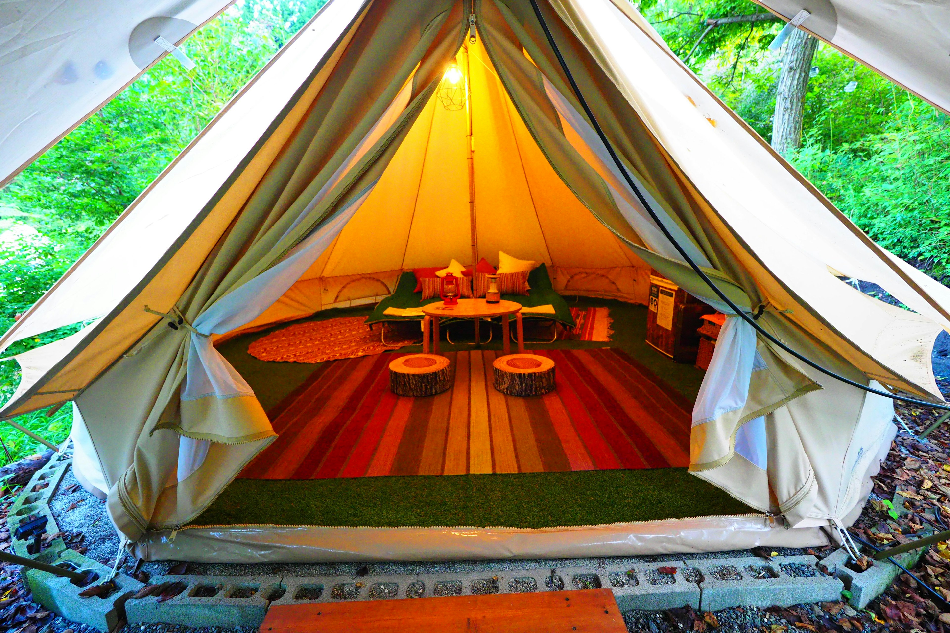 Intérieur d'une tente de glamping entourée de verdure avec des tapis colorés et des meubles