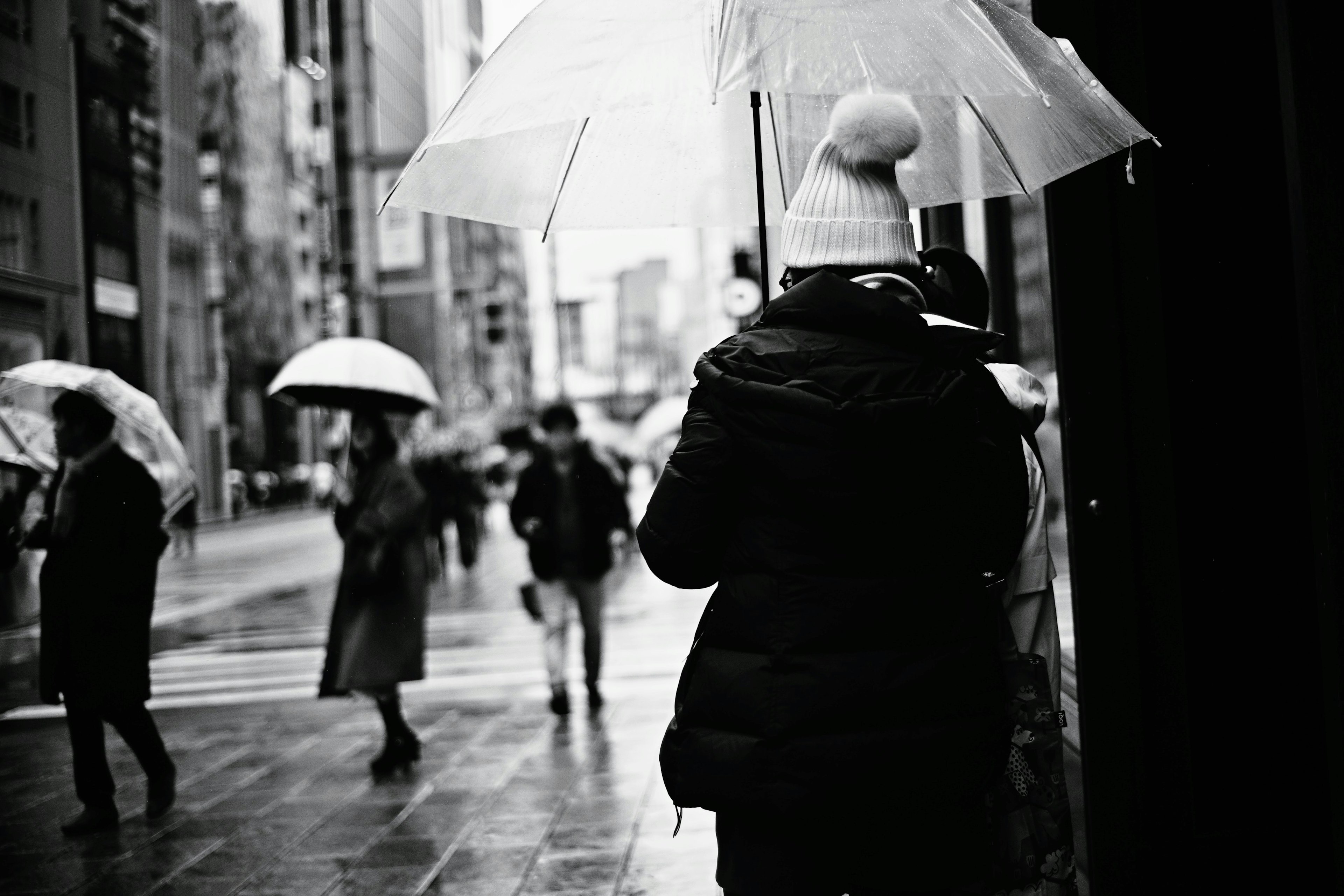 Des personnes tenant des parapluies par un jour de pluie dans un cadre urbain en noir et blanc