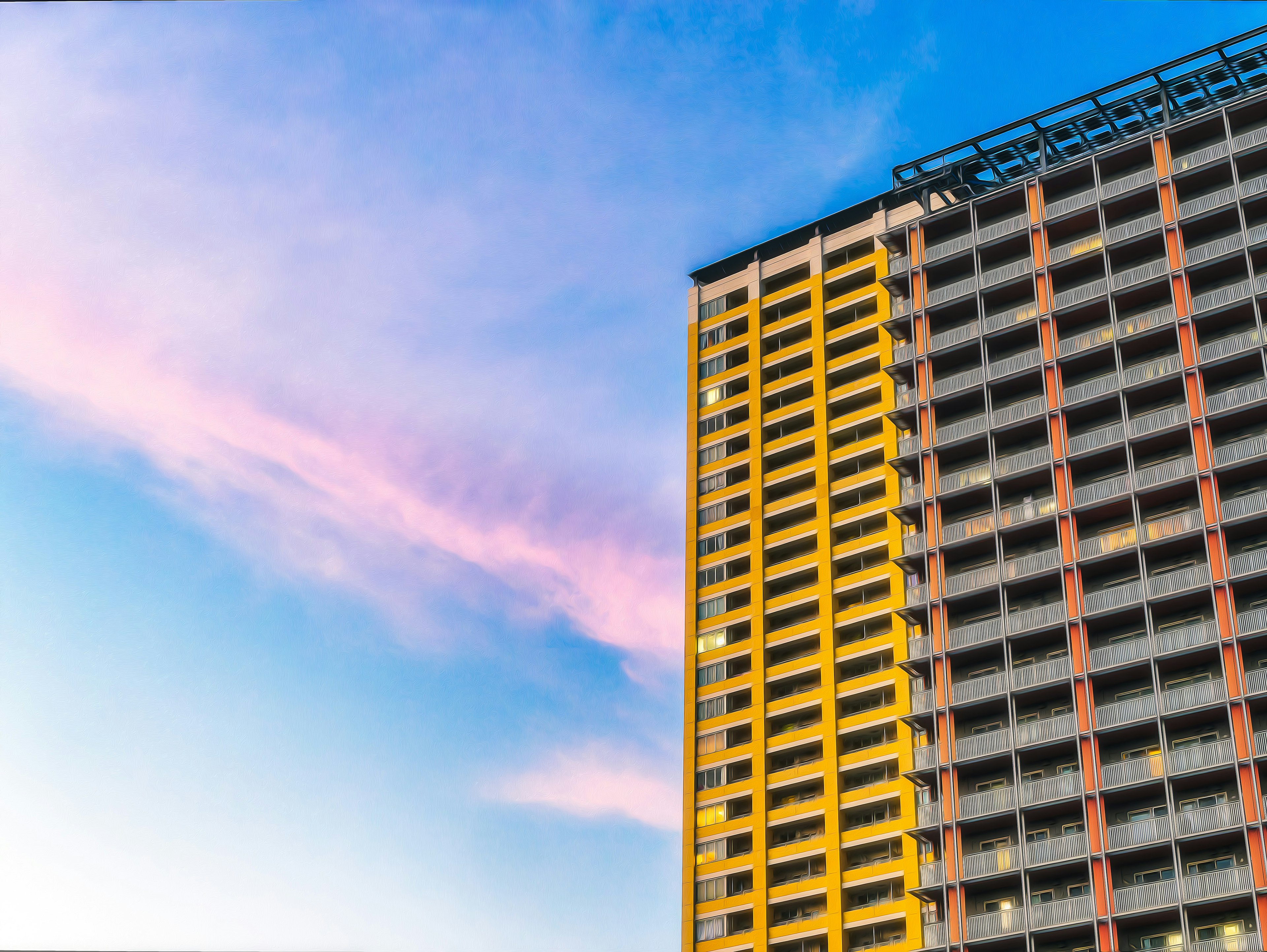 Part of a high-rise building against a blue sky with yellow exterior and pink clouds