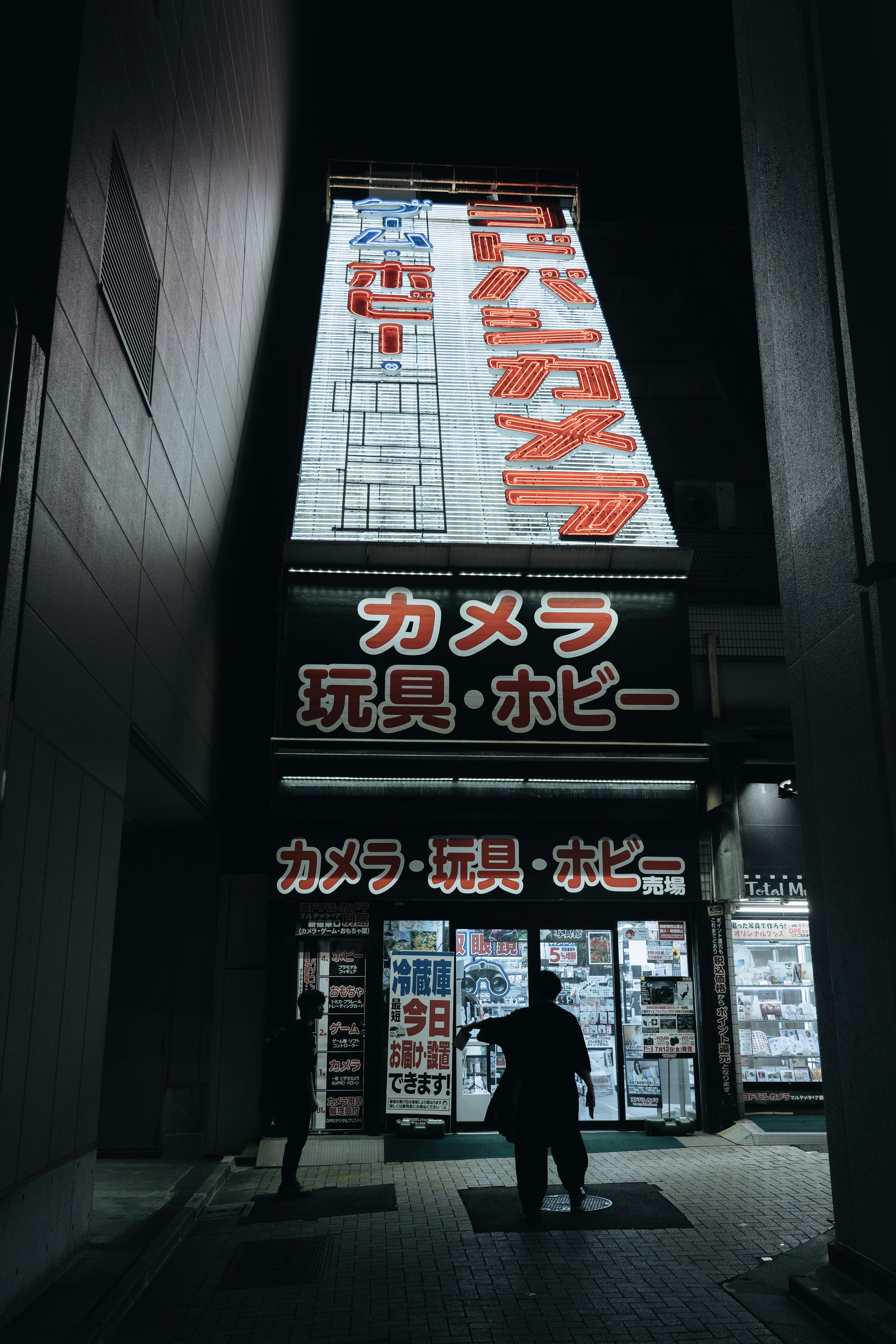 Nighttime storefront of a camera and hobby shop with bright signage