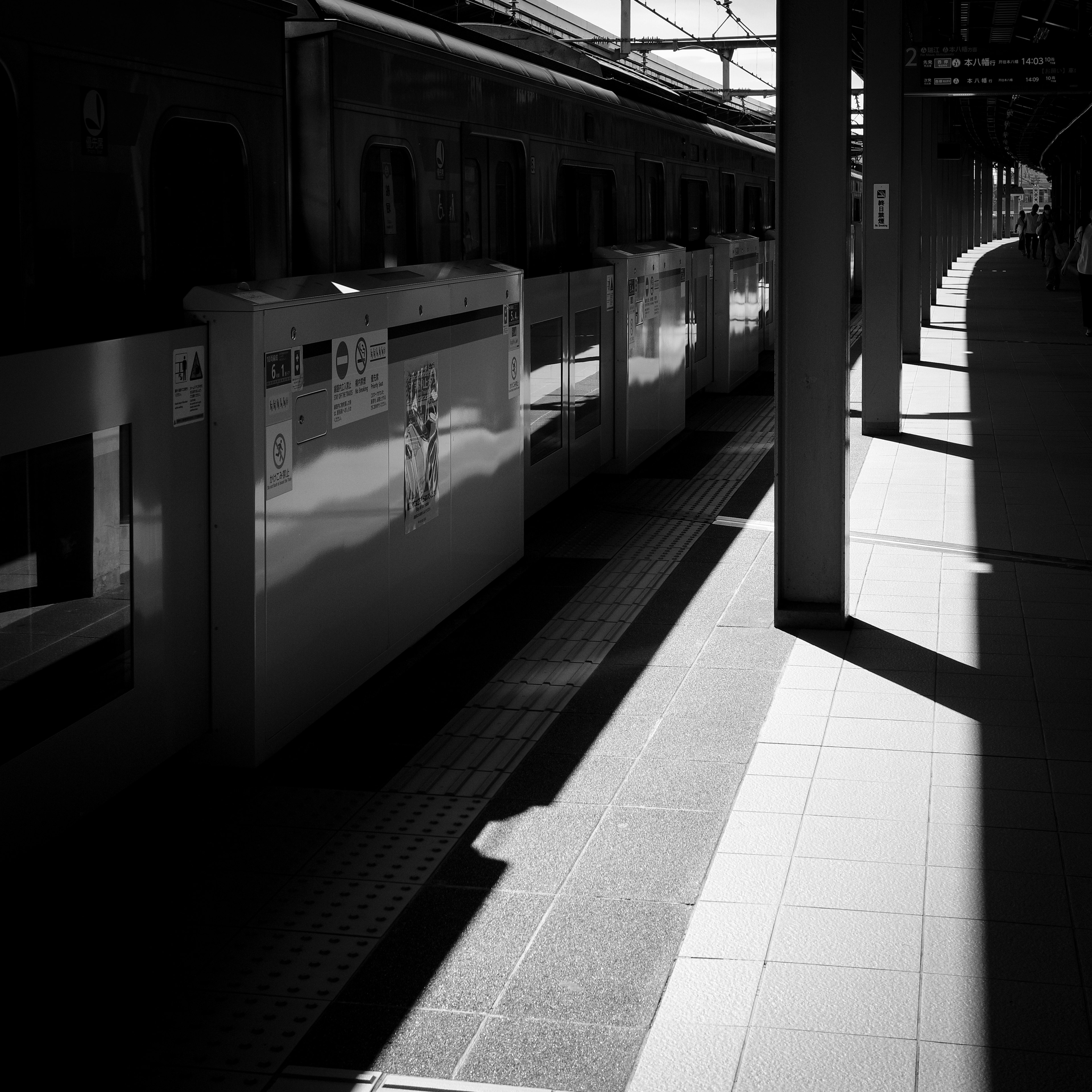 ภาพขาวดำของชานชาลารถไฟที่มีตู้รถไฟและเงา