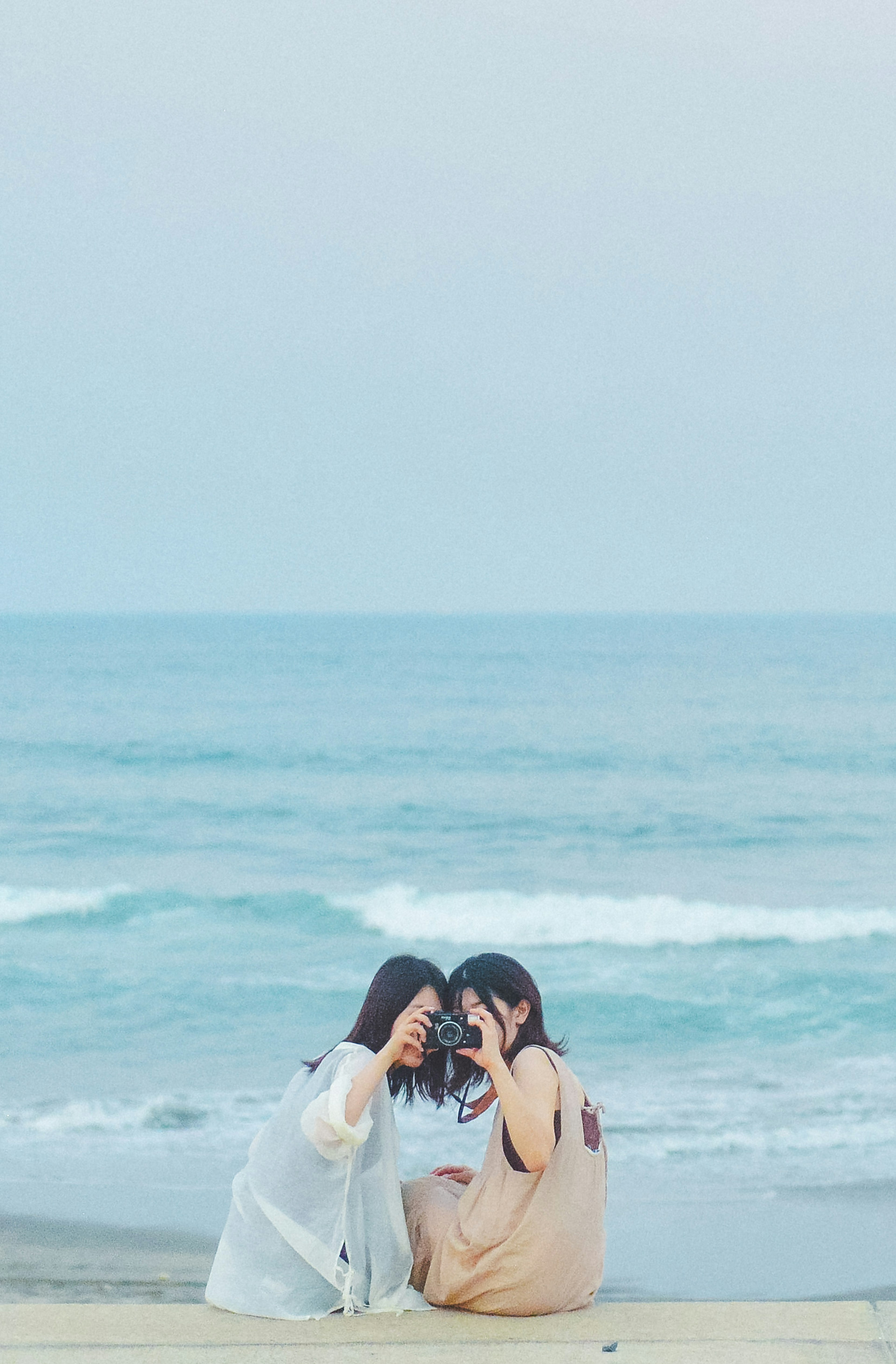 Two women posing playfully with a camera by the seaside