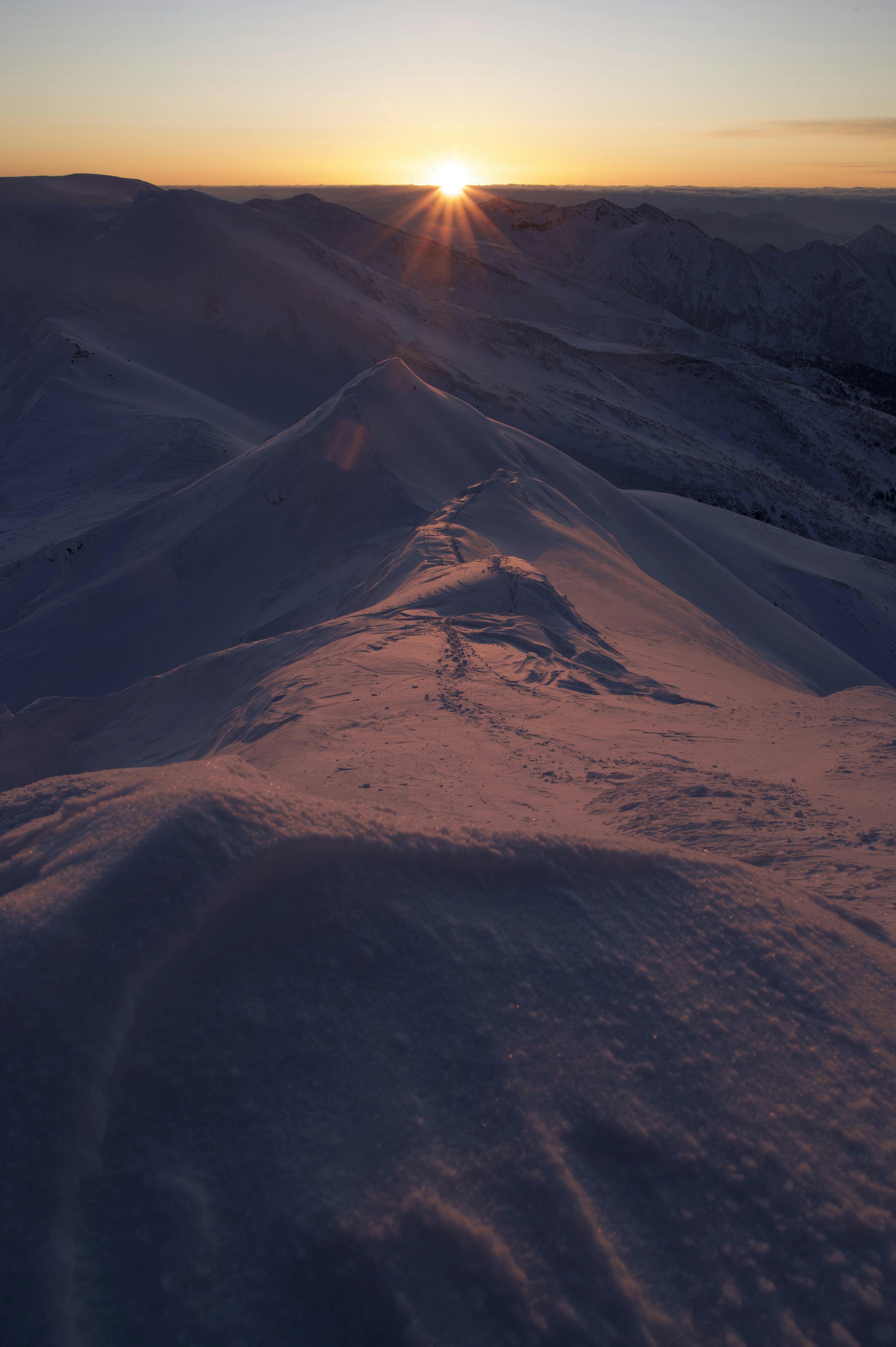 雪に覆われた丘陵の上に昇る太陽の光景