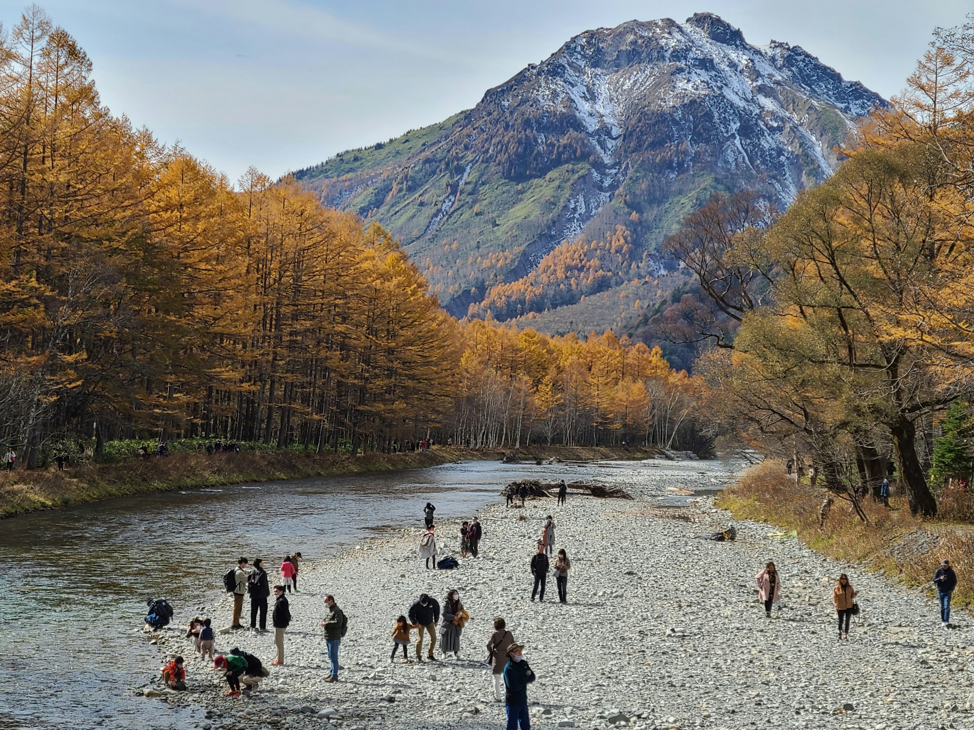 美しい山とオレンジ色の木々に囲まれた川で遊ぶ人々