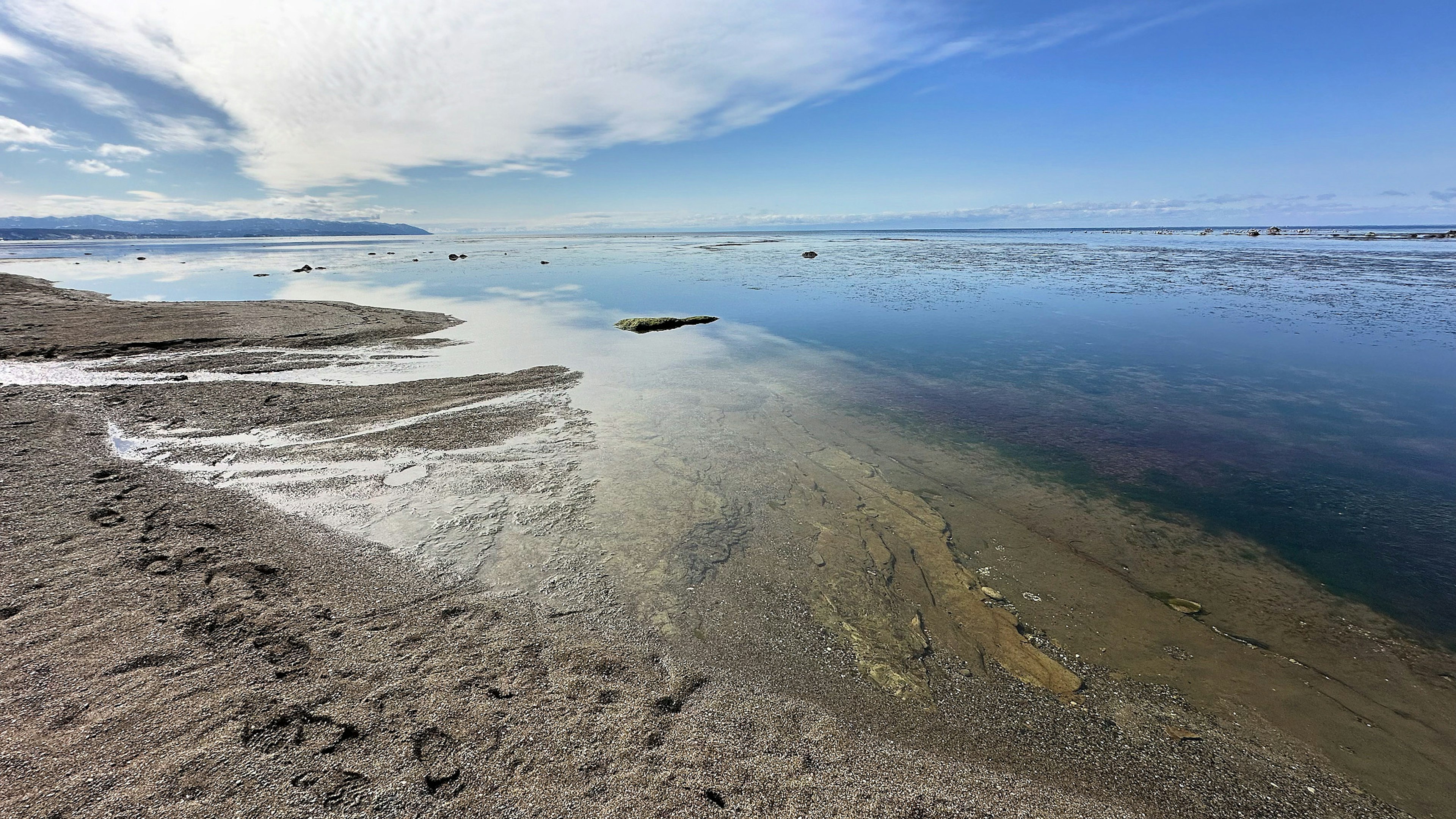 Serene beach landscape with blue sky and cloud reflections on the water